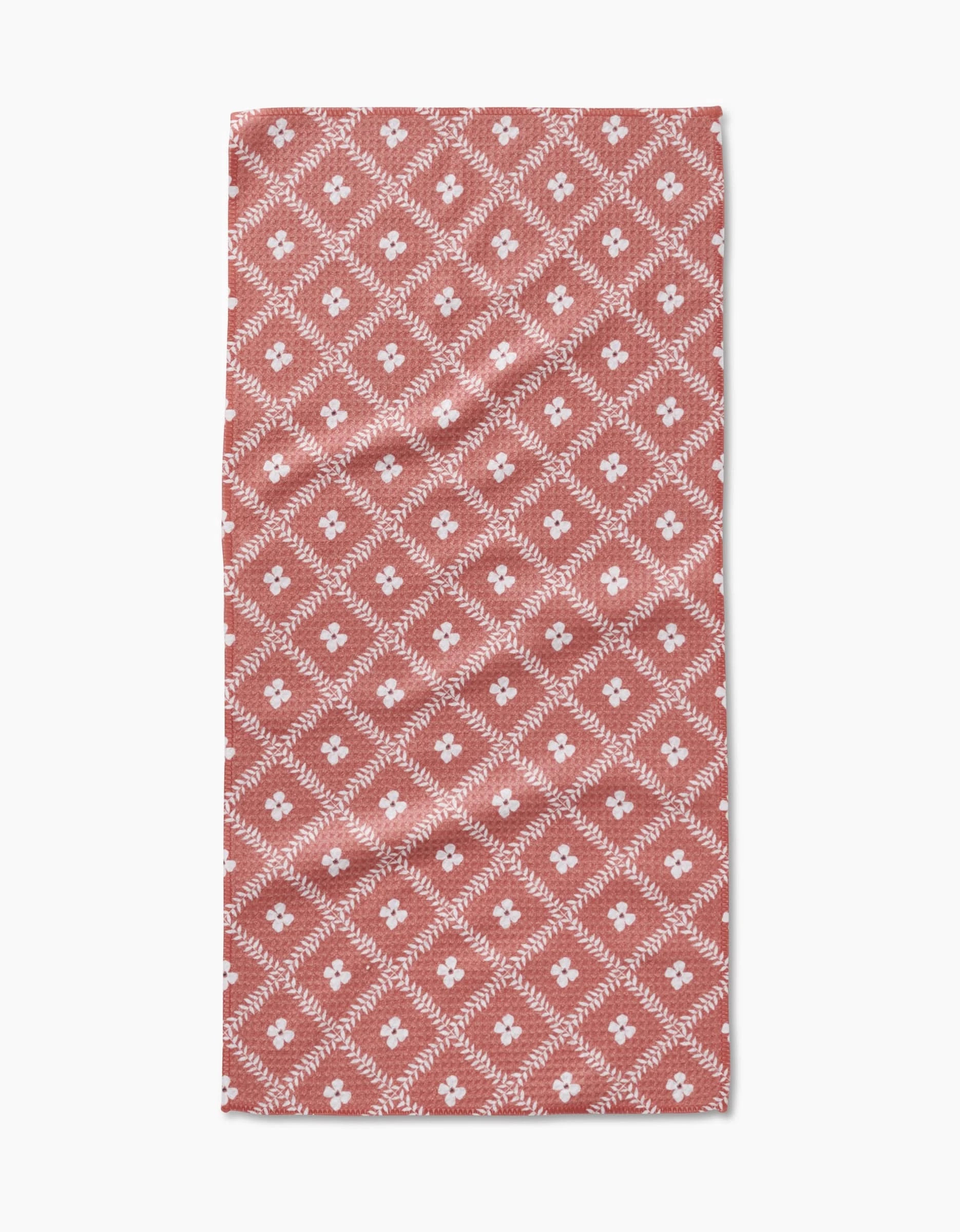 Charlie Rowan Designs’ Floral Lattice Bar Towel showcases a red background with a repeating white diamond pattern, each centered with a white flower. The symmetrical design is crafted from Geoweave fabric for durability and style.