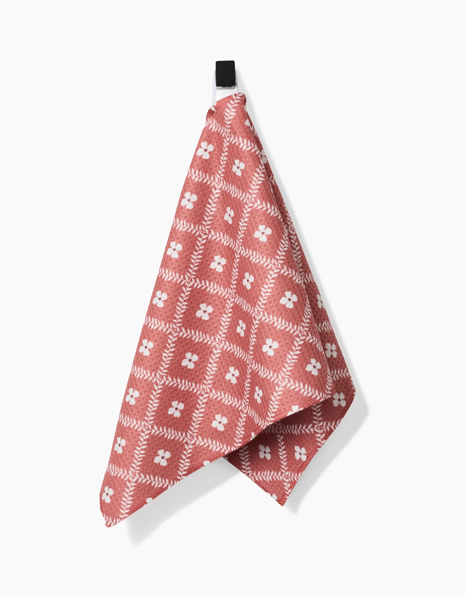 The Floral Lattice bar towel by Charlie Rowan Designs features a red and white geometric floral pattern, hangs from a black hook on a white background, and is crafted from durable Geoweave fabric.