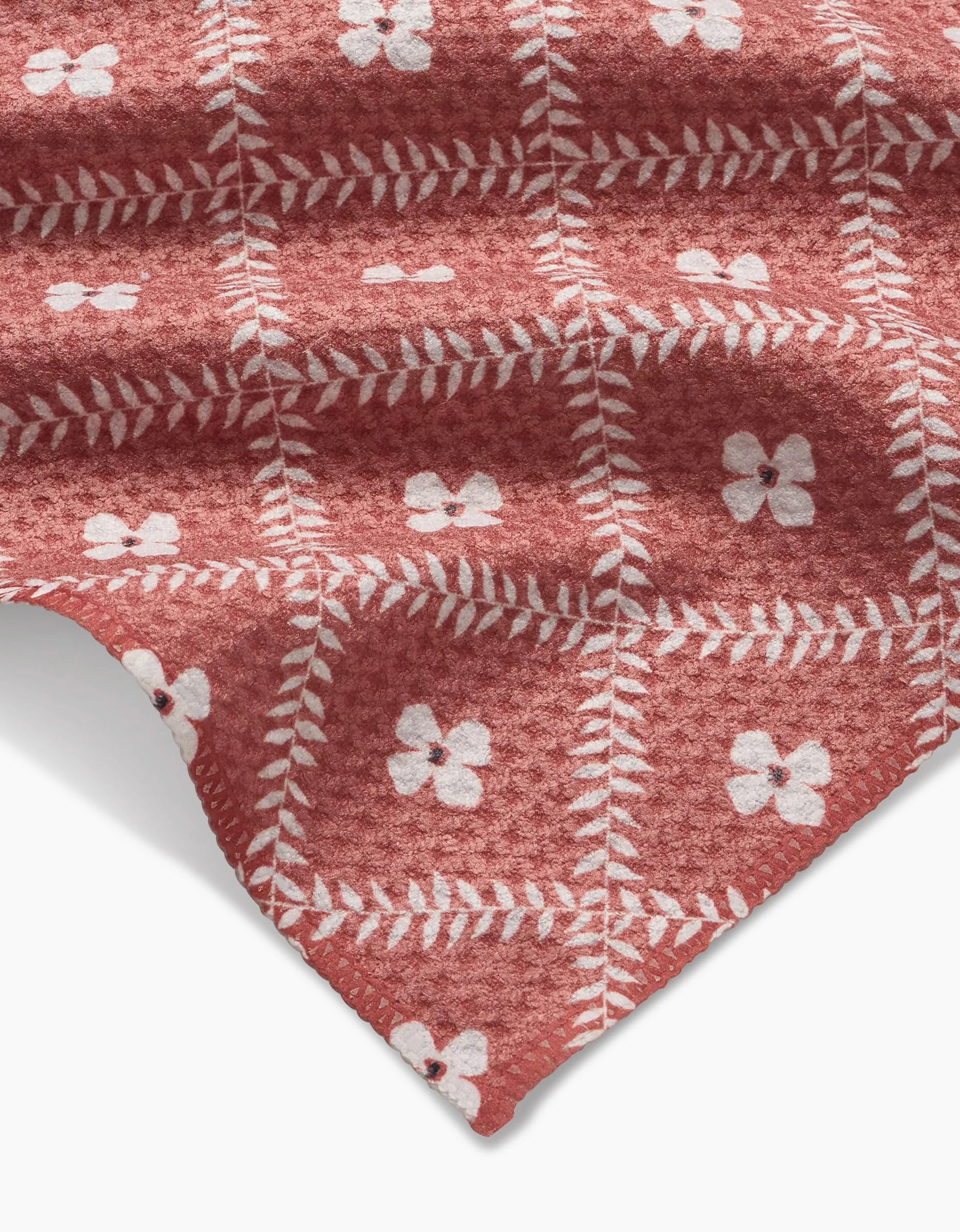 The Floral Lattice blanket by Charlie Rowan Designs features a reddish-pink Geoweave fabric with a grid pattern and white floral motifs, offering a soft, cozy look against a white background.