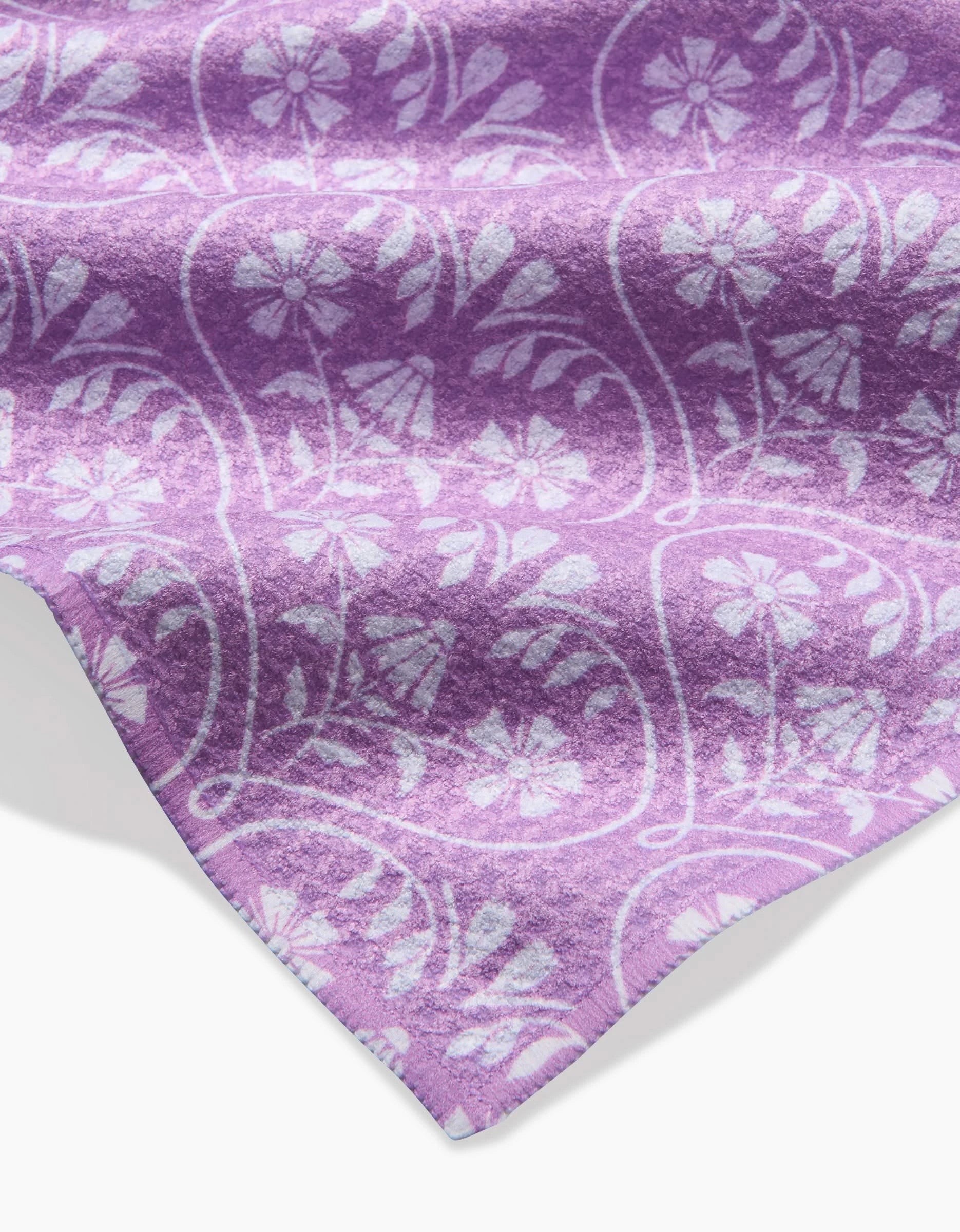 A close-up of Hufton Studios Floral Vine Hearts bar towel in purple Geoweave fabric, featuring a white floral and leaf pattern, wavy edge, and a light shadow on a white background.