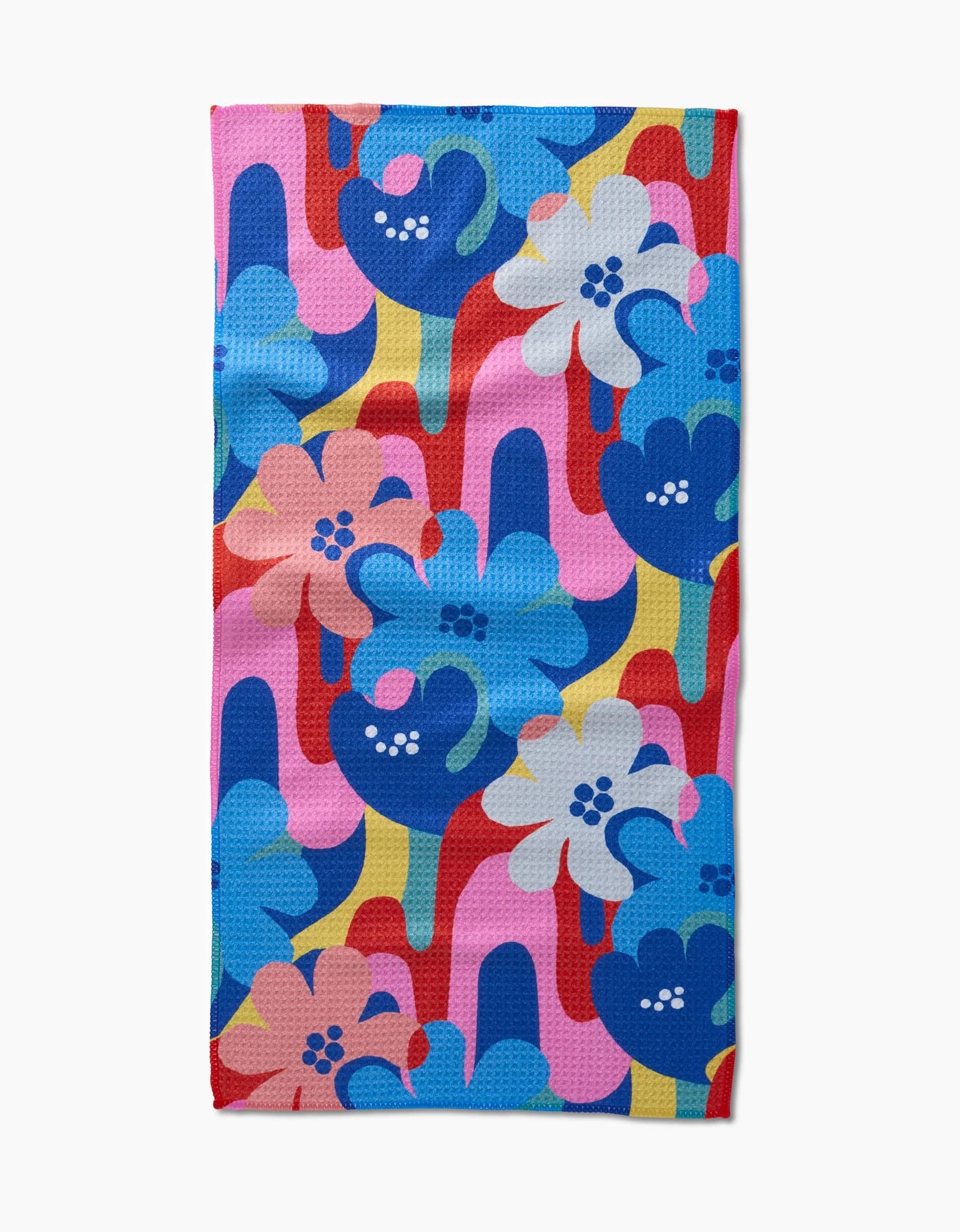 Flower Powers by Masha Volnova is a rectangular bar towel made from recycled materials, displaying bold blue, pink, white, and red flowers atop overlapping pink, yellow, red, and blue shapes.