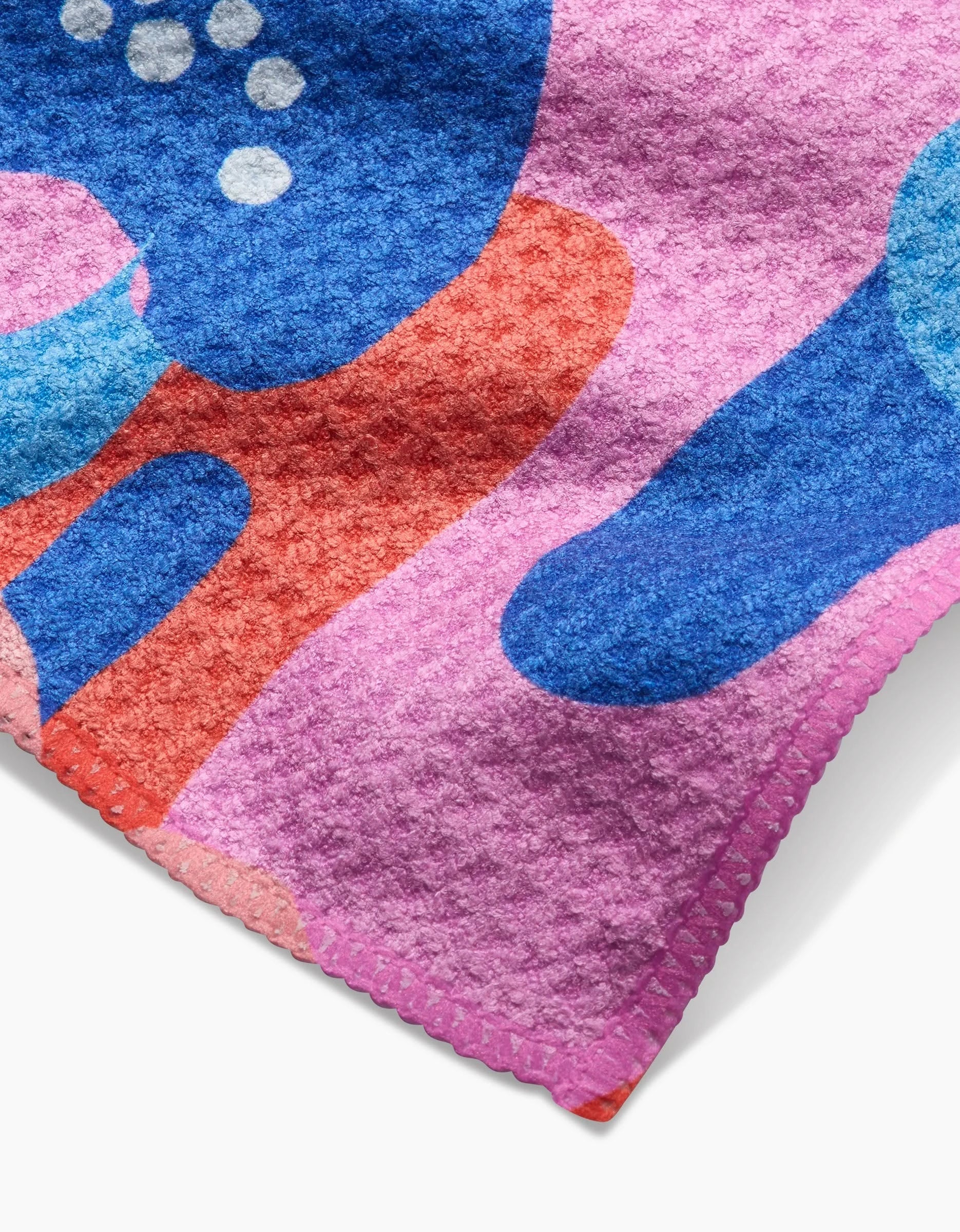 A close-up of the Flower Powers Bar Towel by Masha Volnova, crafted from recycled materials, with pink, blue, orange, and white abstract shapes and scalloped edge stitching.