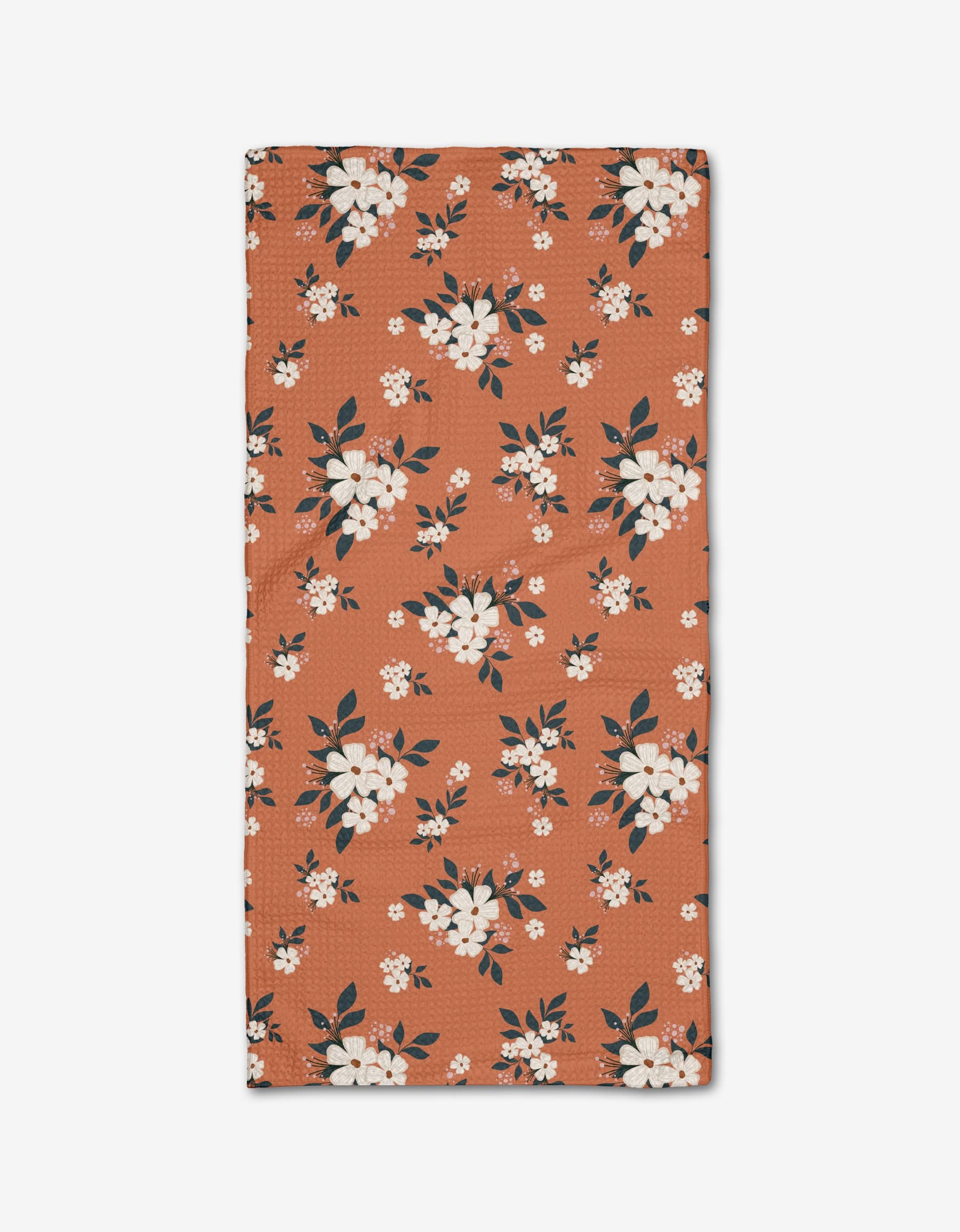 The Flowers in the Field bar towel by Charlie Rowan Designs is rectangular and rust-colored, made from Geoweave fabric, with white and light pink flowers and dark green leaves scattered across its surface.