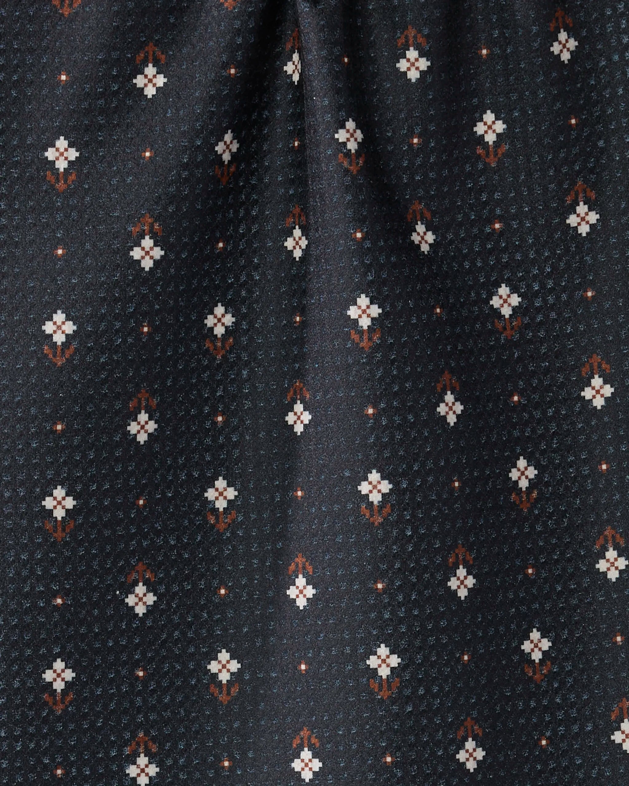 Close-up of Geometry’s Folk Pixel fabric in black, made from recycled materials with a repeating small white and orange floral pattern—subtle diagonal rows and a central fold add depth, ideal for an ultra-absorbent towel or bar towel.