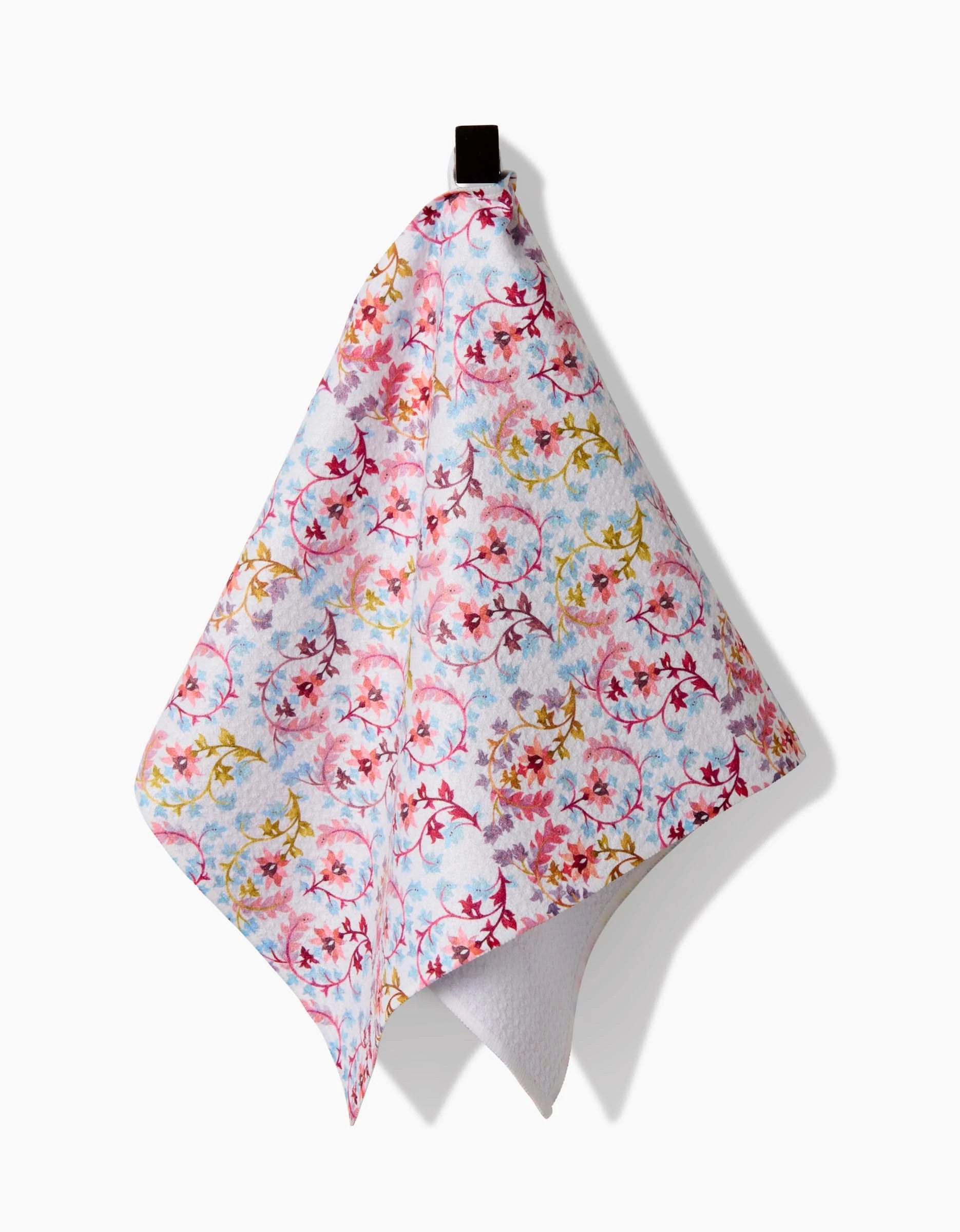 The Maayan Alper-Swan Folk Tapestry towel features a colorful floral pattern in red, pink, yellow, and blue on soft Geoweave fabric, and hangs from a black loop against a white background.