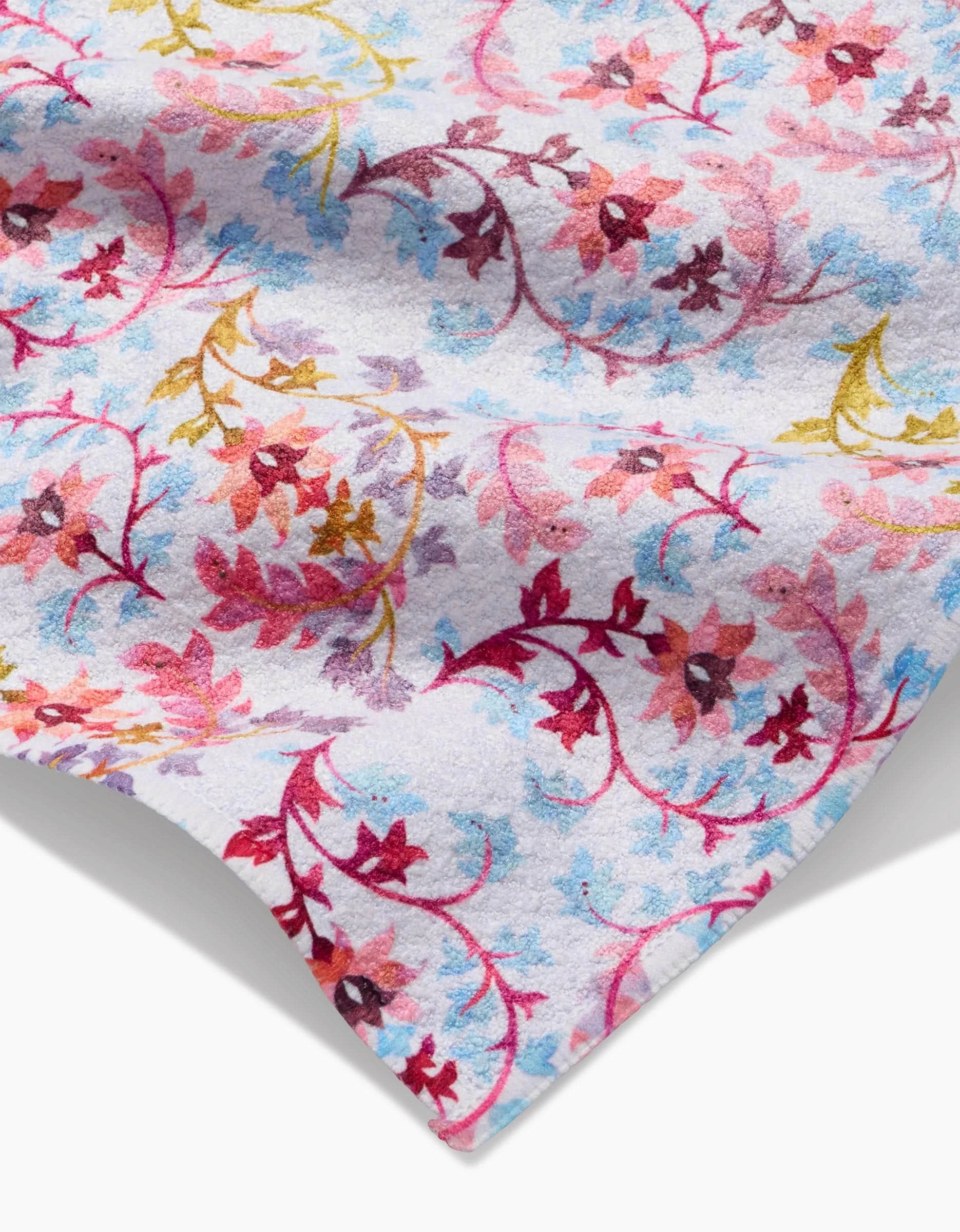 A close-up of the Maayan Alper-Swan Folk Tapestry bar towel, made from recycled Geoweave fabric, features a colorful floral pattern—red, pink, blue, and yellow flowers with vines on white—showcasing its quality and textured finish.