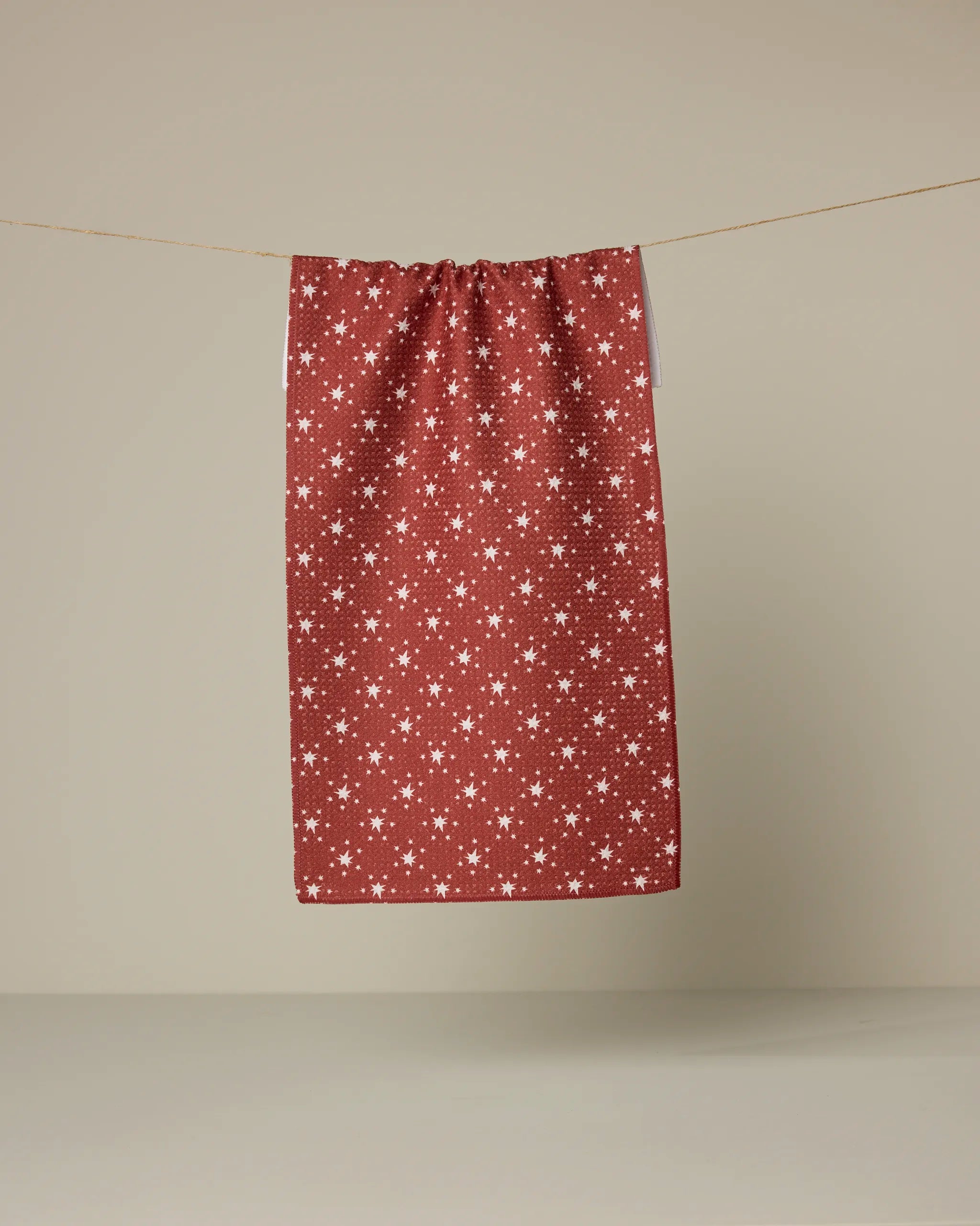 Freedom Red, a recycled kitchen towel by Geometry featuring a white star pattern, hangs on a thin line against a plain beige background.