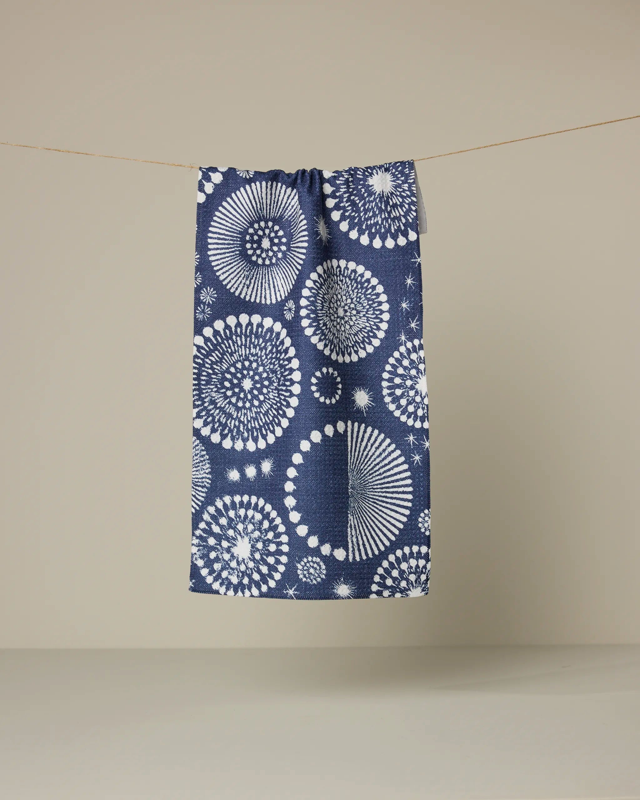 The Geometry Freedom Sparks Navy towel, featuring ultra-absorbent fabric and white mandala-inspired circles, hangs from a thin line against a plain beige background.