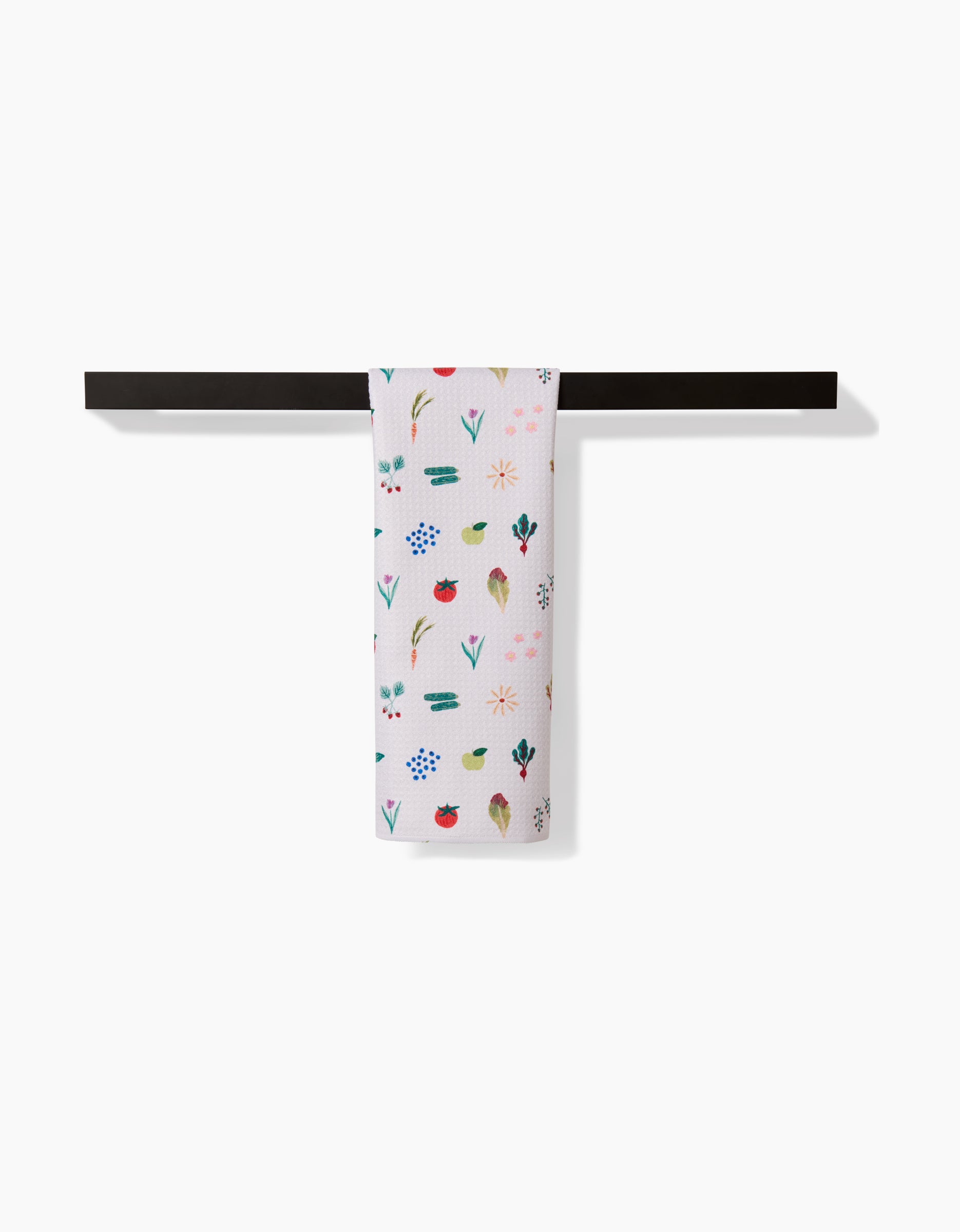 The Brittany Jepsen Fresh Produce dish towel, made from ultra-absorbent Geoweave fabric and featuring colorful floral and leaf patterns, hangs neatly on a black rod against a plain white background.
