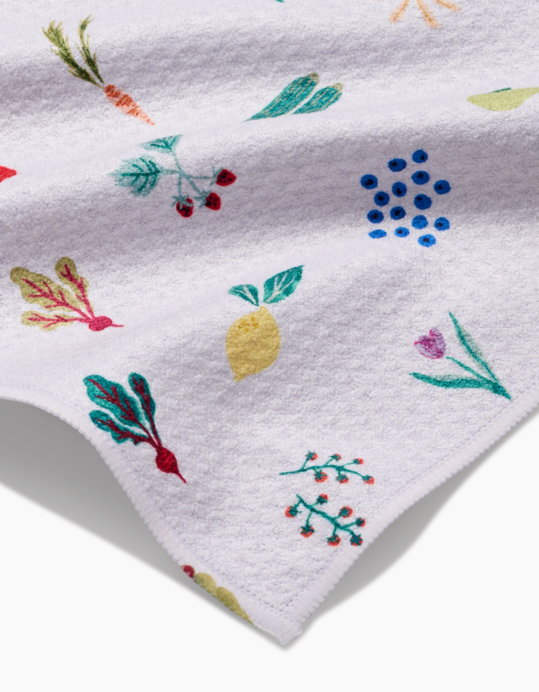 The Brittany Jepsen Fresh Produce towel features ultra-absorbent white Geoweave fabric adorned with colorful embroidered fruits, vegetables, and plants—like lemons, carrots, berries, and leafy greens—with a folded corner.