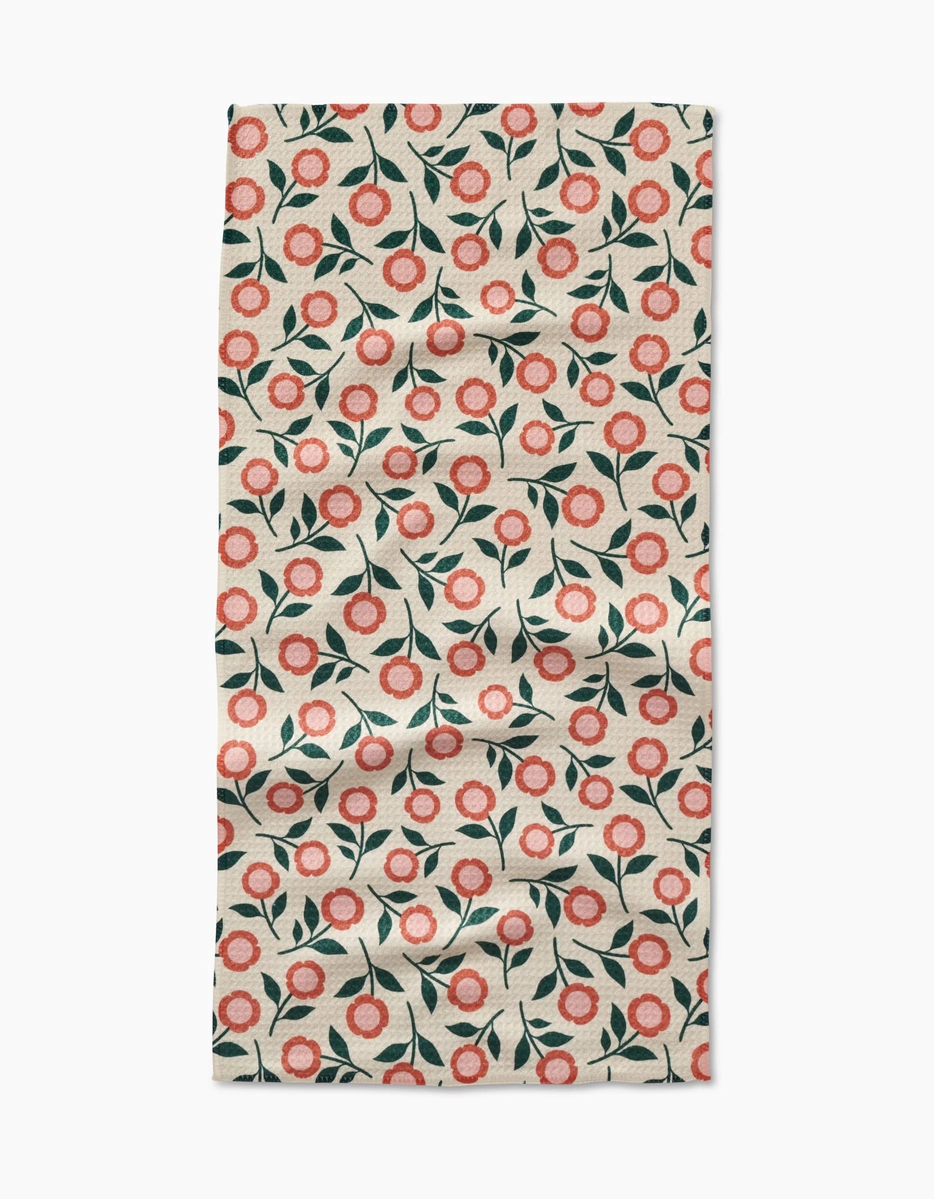 A slightly wrinkled Megan Kampa Friendly Floral Peach Geoweave bar towel, with a repeating red and pink flower and green leaf pattern on cream, is displayed on a white surface.