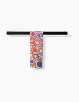 The Claire Iglesias Fruits Party Bar Towel, with a vibrant fruit and flower design in red, blue, purple, and white on soft Geoweave for top absorbency, hangs on a black towel bar against a plain white background.