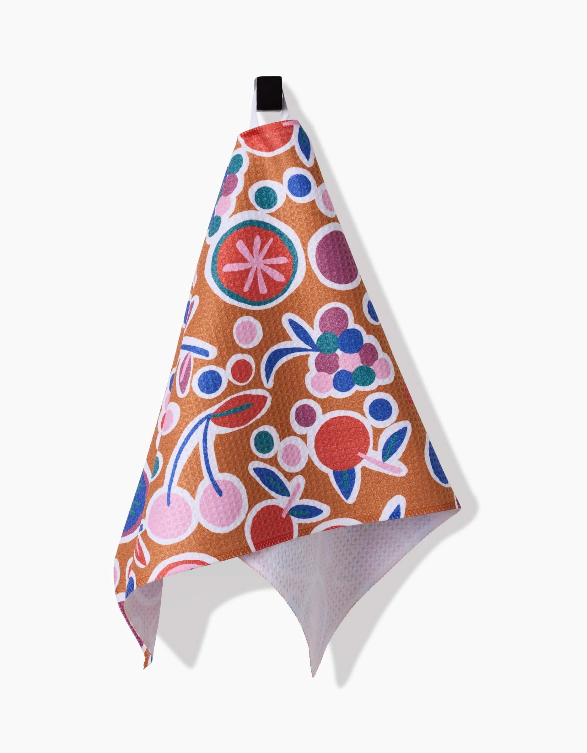 The Claire Iglesias Fruits Party Bar Towel features a vibrant fruit and floral pattern in red, pink, blue, and purple on brown Geoweave fabric, displayed hanging from a black loop against a white background.