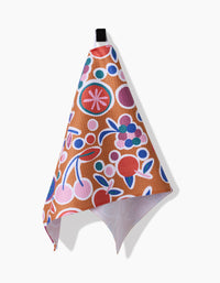 The Claire Iglesias Fruits Party Bar Towel features a vibrant fruit and floral pattern in red, pink, blue, and purple on brown Geoweave fabric, displayed hanging from a black loop against a white background.