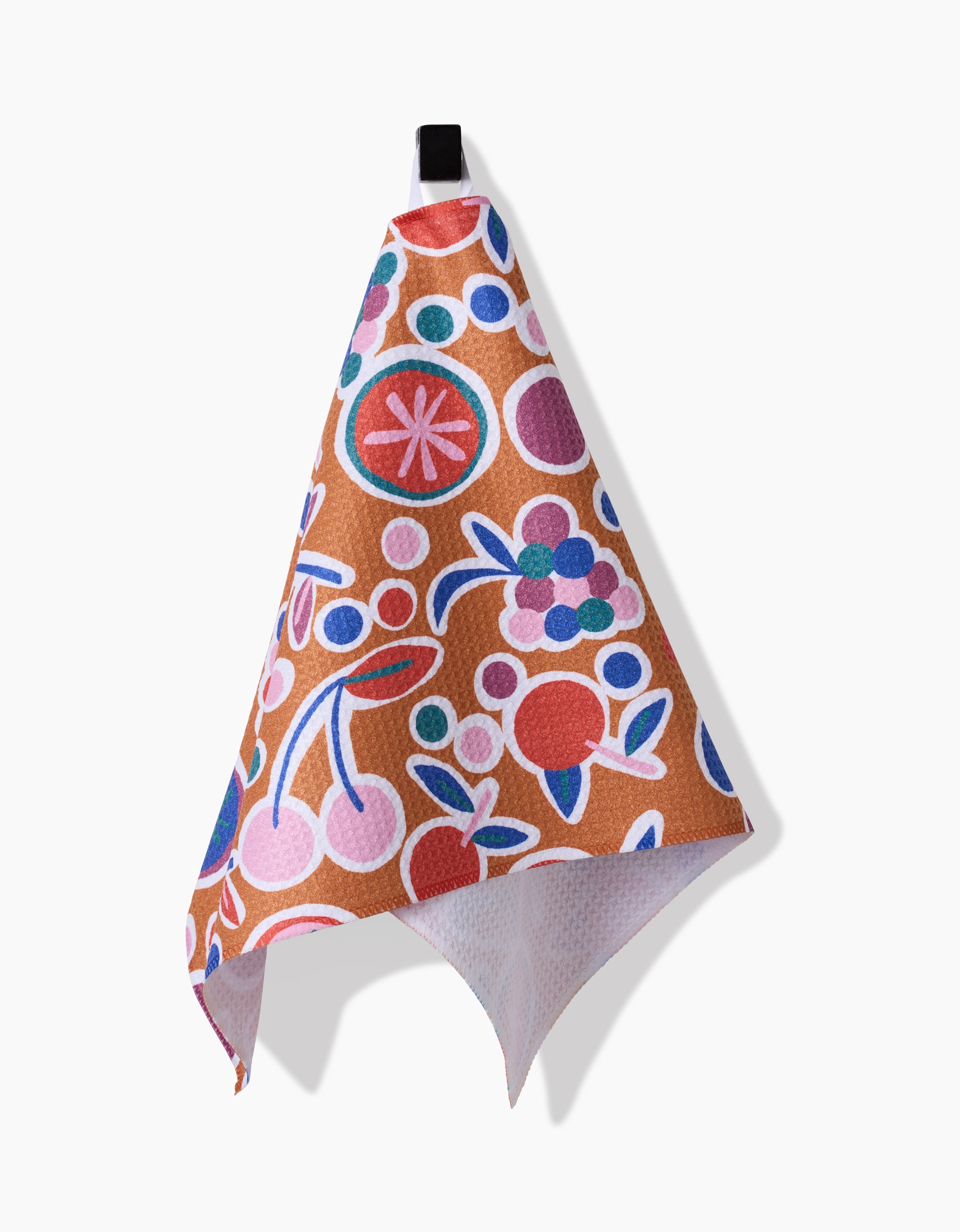 The Claire Iglesias Fruits Party Bar Towel features a vibrant fruit and floral pattern in red, pink, blue, and purple on brown Geoweave fabric, displayed hanging from a black loop against a white background.