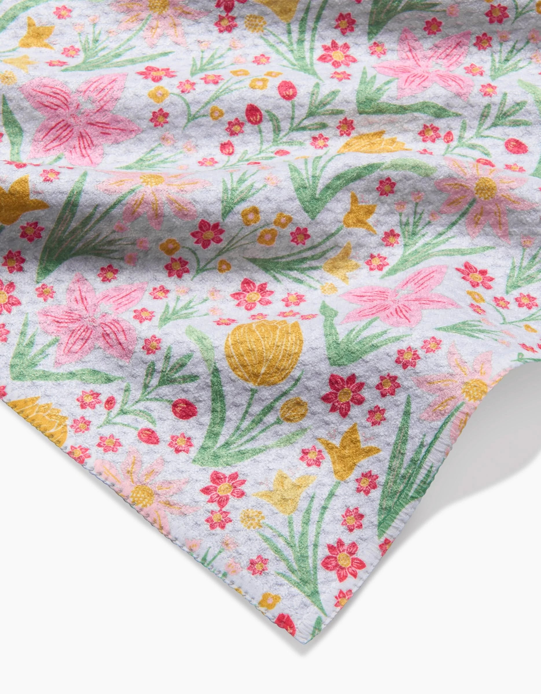 The “Garden of Light” by Danelys Sidron is a soft, white Geoweave fabric cloth showcasing a vibrant floral pattern with pink, yellow, and red flowers and green leaves on a white background, gently folded at the corner.