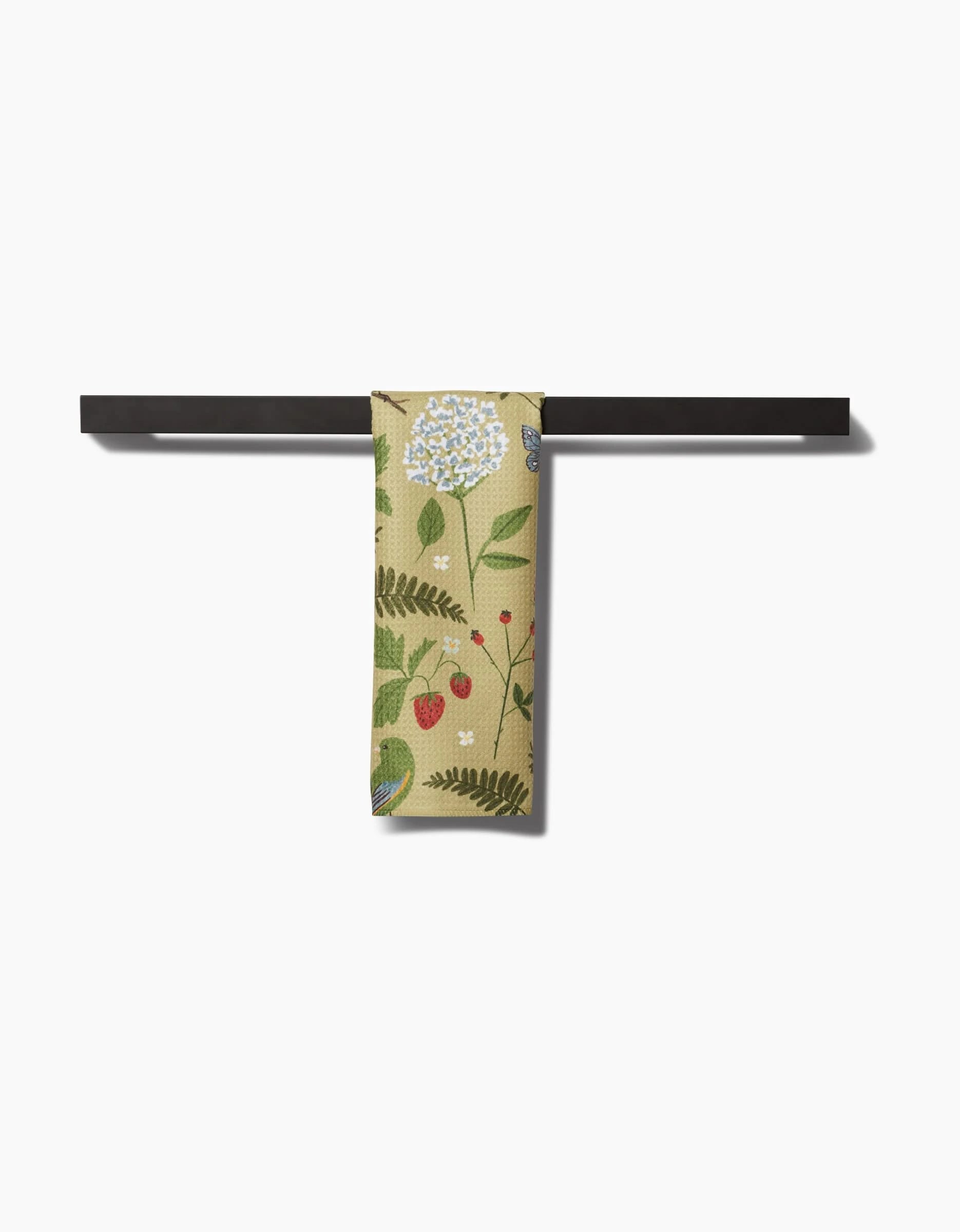 The Good Green Earth bar towel by Janna Sue Design features a botanical pattern and hangs on a sleek black bar. Crafted from Geoweave fabric, it stands out against the white background.