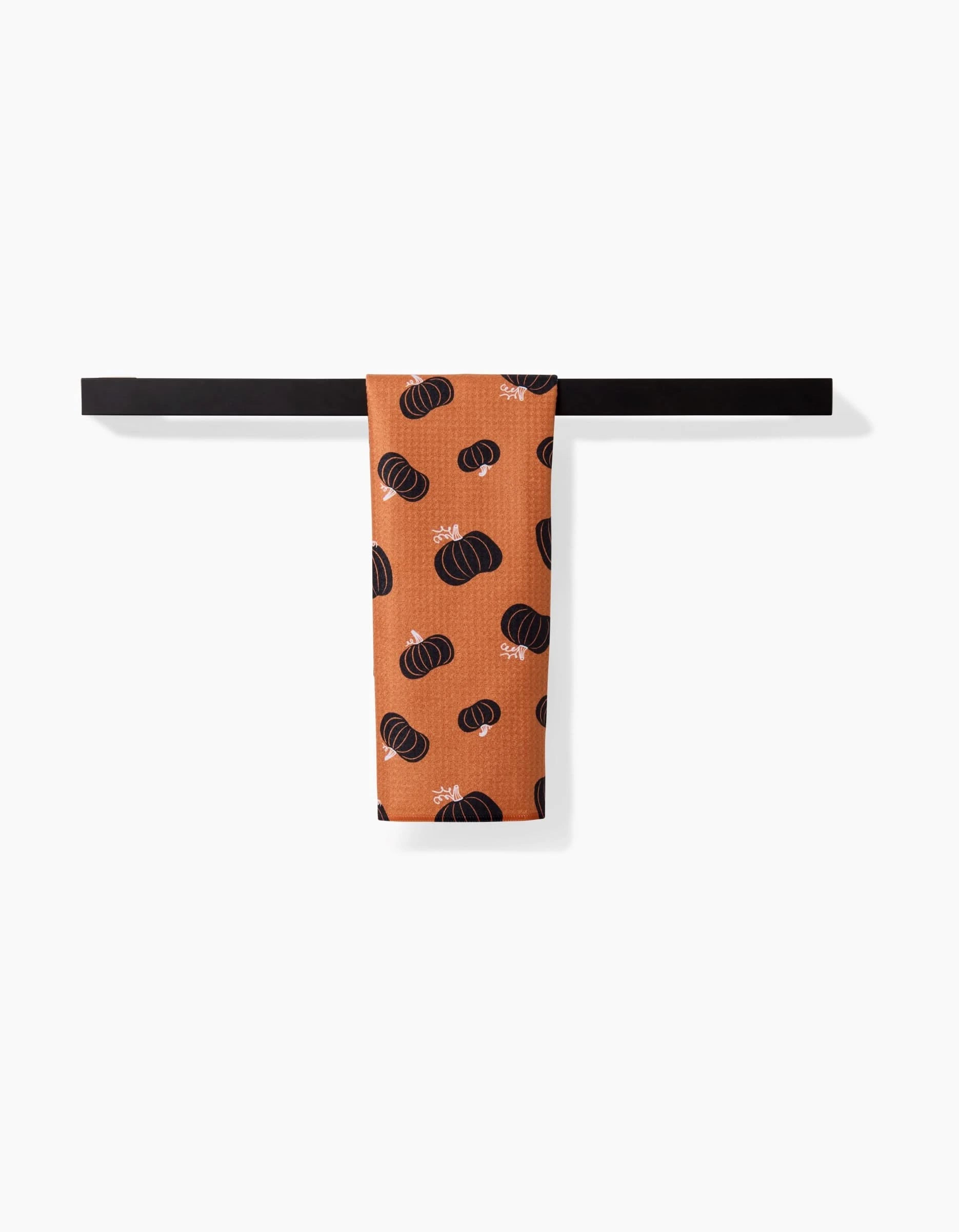 The Halloween Black Pumpkins bar towel by Hufton Studio, featuring black pumpkin patterns and made from recycled materials, hangs neatly on a black bar against a white backdrop.