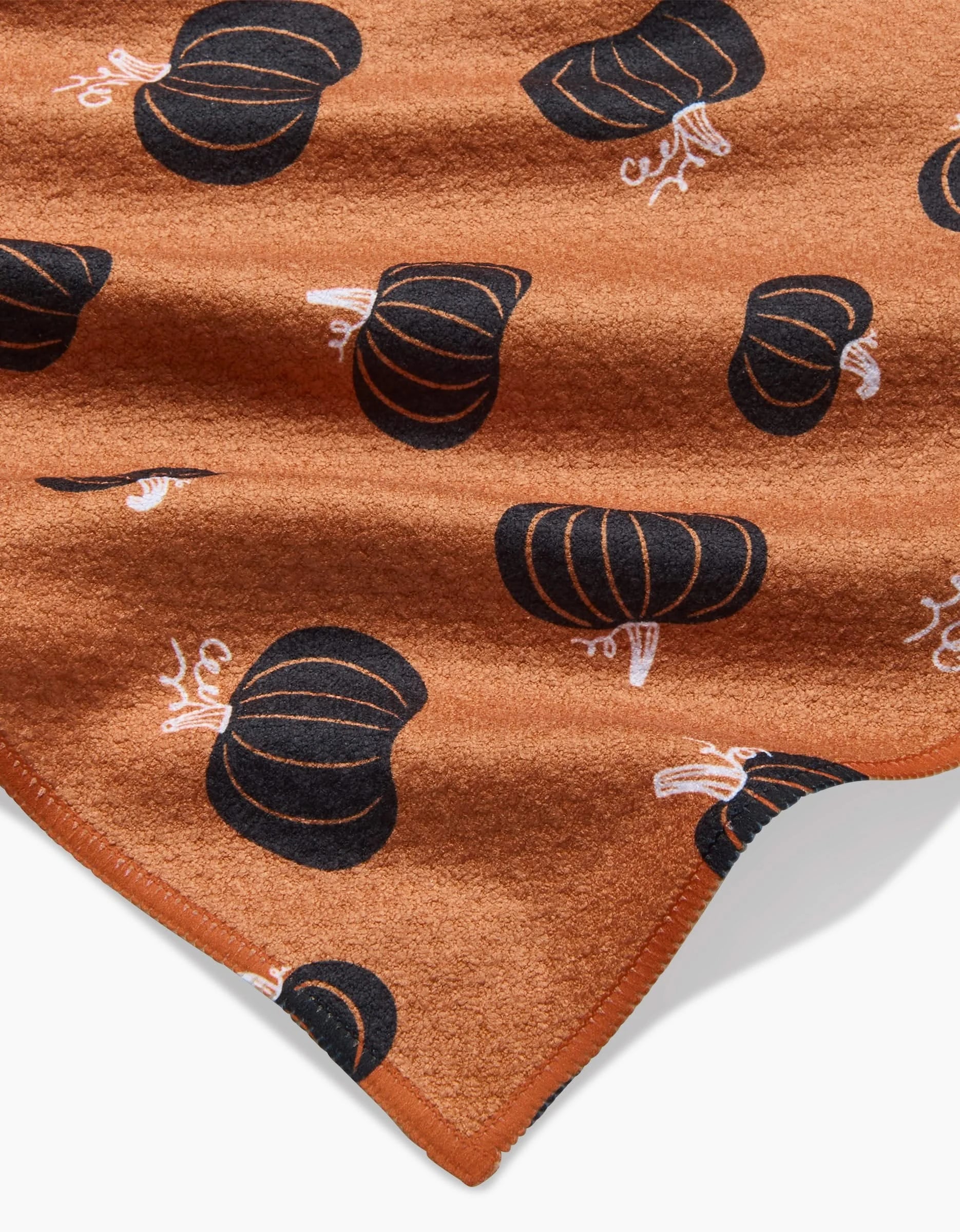 The Hufton Studio Halloween Black Pumpkins blanket features black pumpkin patterns with white stems on brown fabric, a stitched edge, and is made from recycled materials. The soft blanket is shown partially folded.