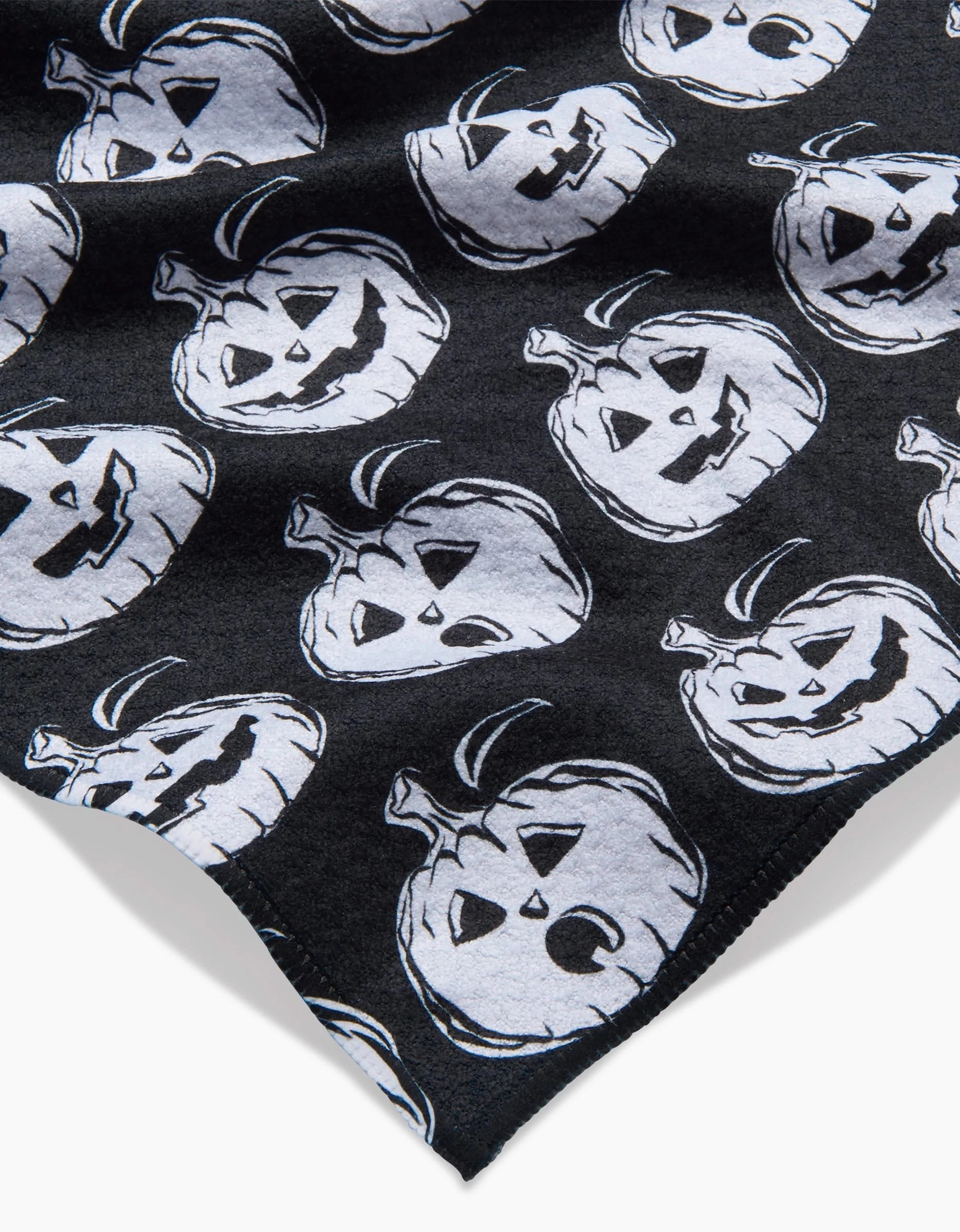 The Aubrey Fairchild Halloween Pumpkins towel is black and ultra-absorbent, featuring white, sketch-style jack-o-lantern faces with unique expressions in a playful, repeating pattern.