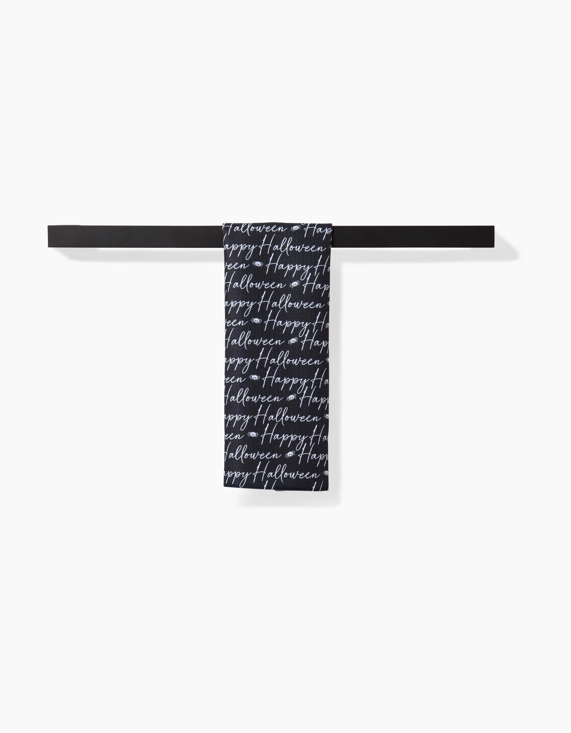 The Geometry Halloween Script Black features a black bar towel holder with an ultra-absorbent towel draped over it, adorned with repeated white cursive Happy Halloween text, set against a plain white background.