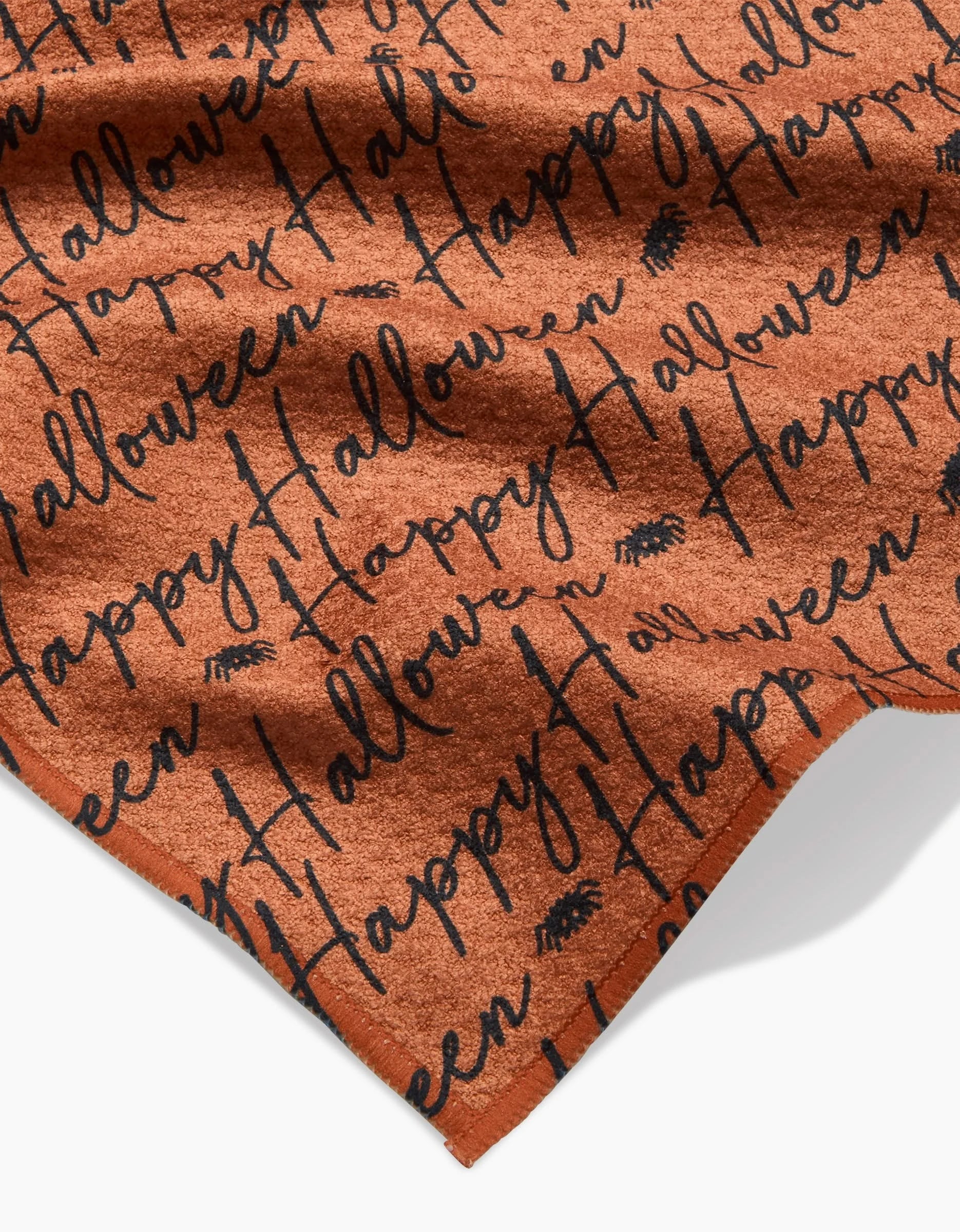 A close-up of the Geometry Halloween Script Orange ultra-absorbent towel with black Happy Halloween script and small spider illustrations.