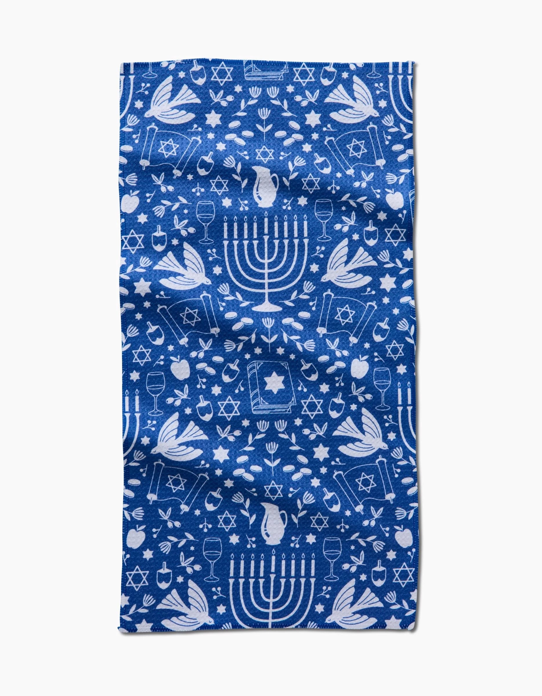The Hanukkah Sameach by Megan Kampa is a blue recycled kitchen towel with white Hanukkah motifs—menorahs, dreidels, doves, Stars of David, gelt coins, and olive branches—perfect as an ultra-absorbent bar towel for festive celebrations.