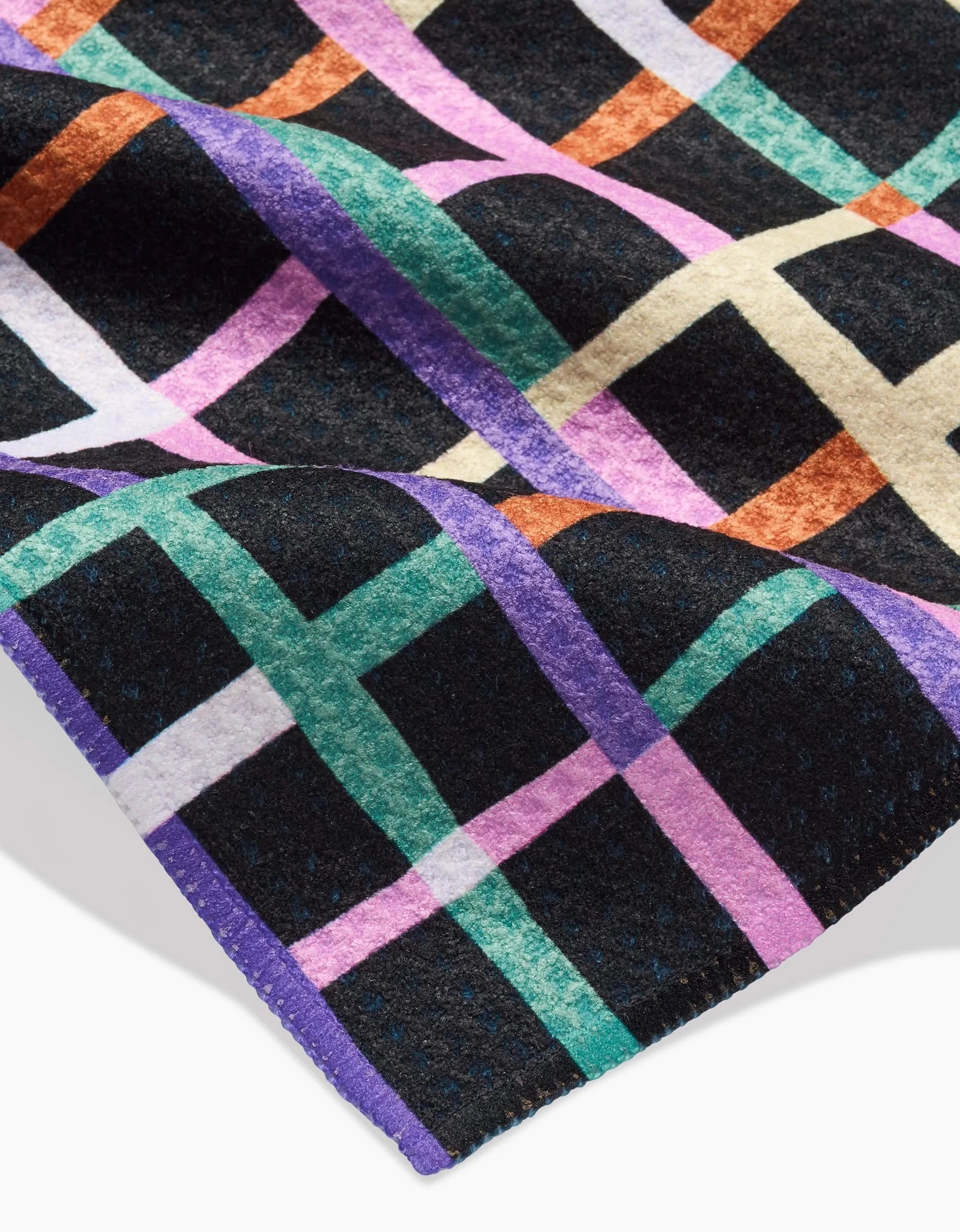 A close-up of Claire Iglesias Happy Plaid Bar Towel shows colorful intersecting lines in purple, teal, orange, and white on black Geoweave fabric, with stitched purple edging.