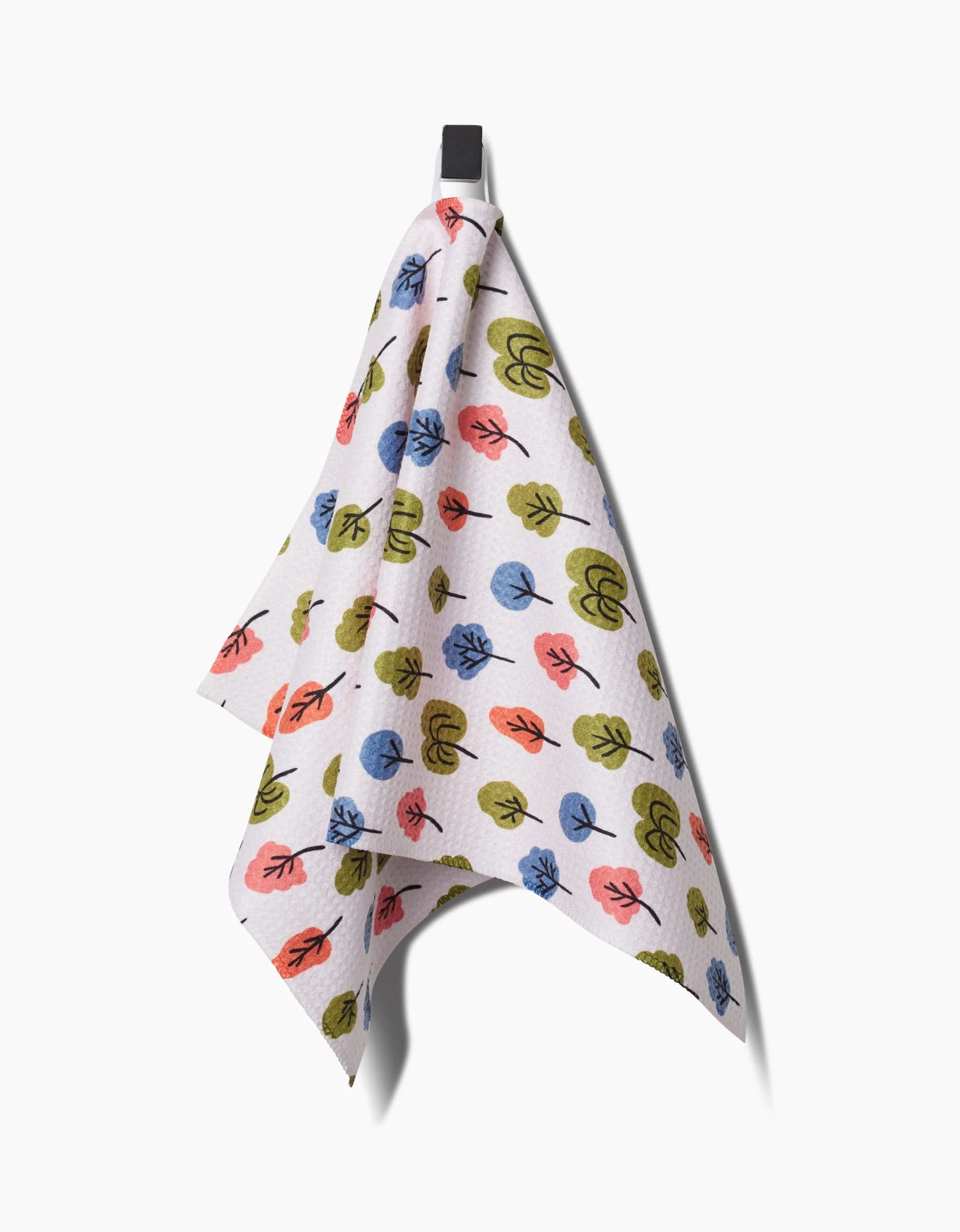 The Kayla Ann Happy Trees bar towel, featuring a vibrant leaf pattern in blue, green, and red on white Geoweave fabric, hangs from a black hook against a plain white background.