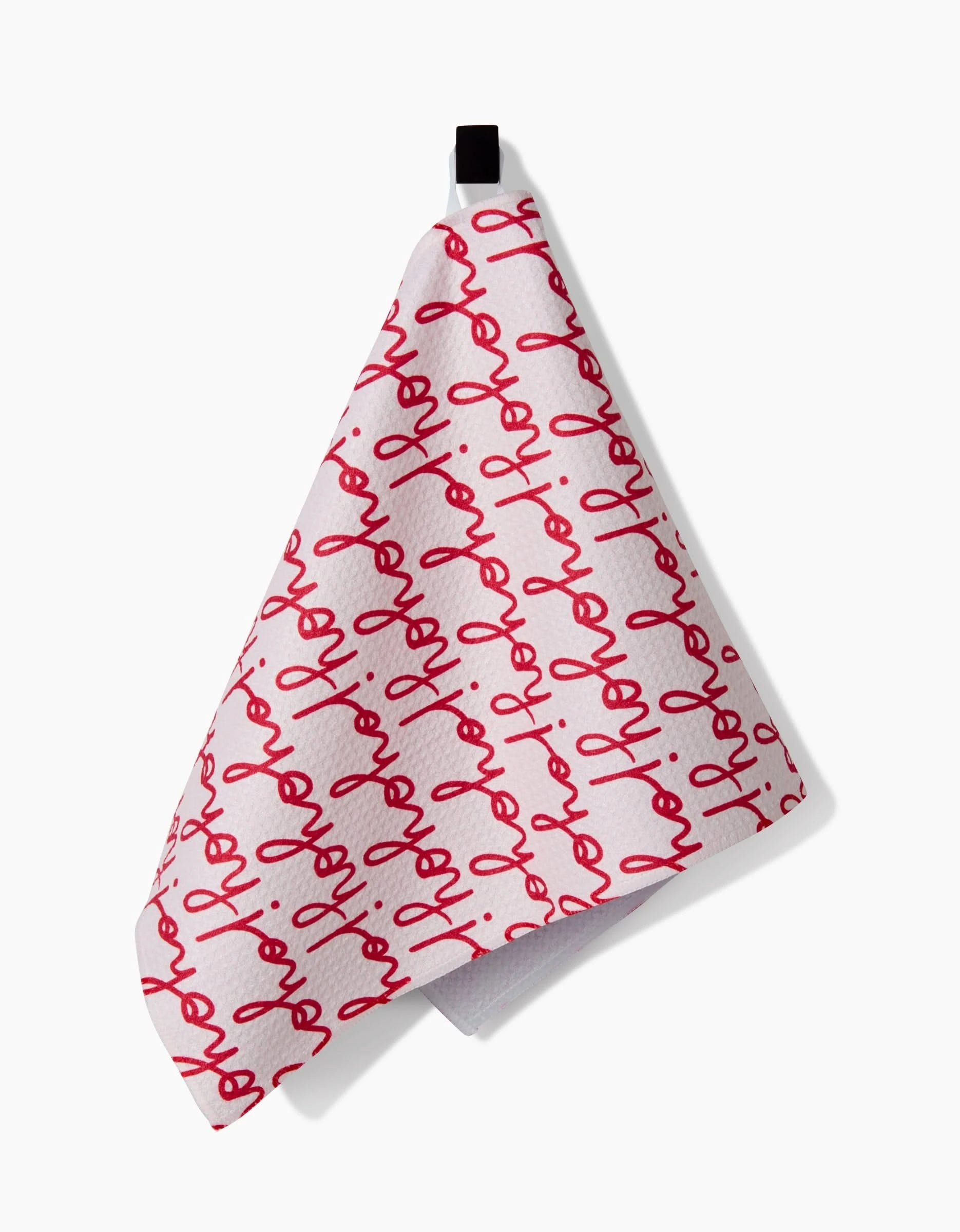 The Kayla Ann Ho Ho Holiday Red kitchen towel is white with a repeating red joy script pattern and hangs by a black loop.