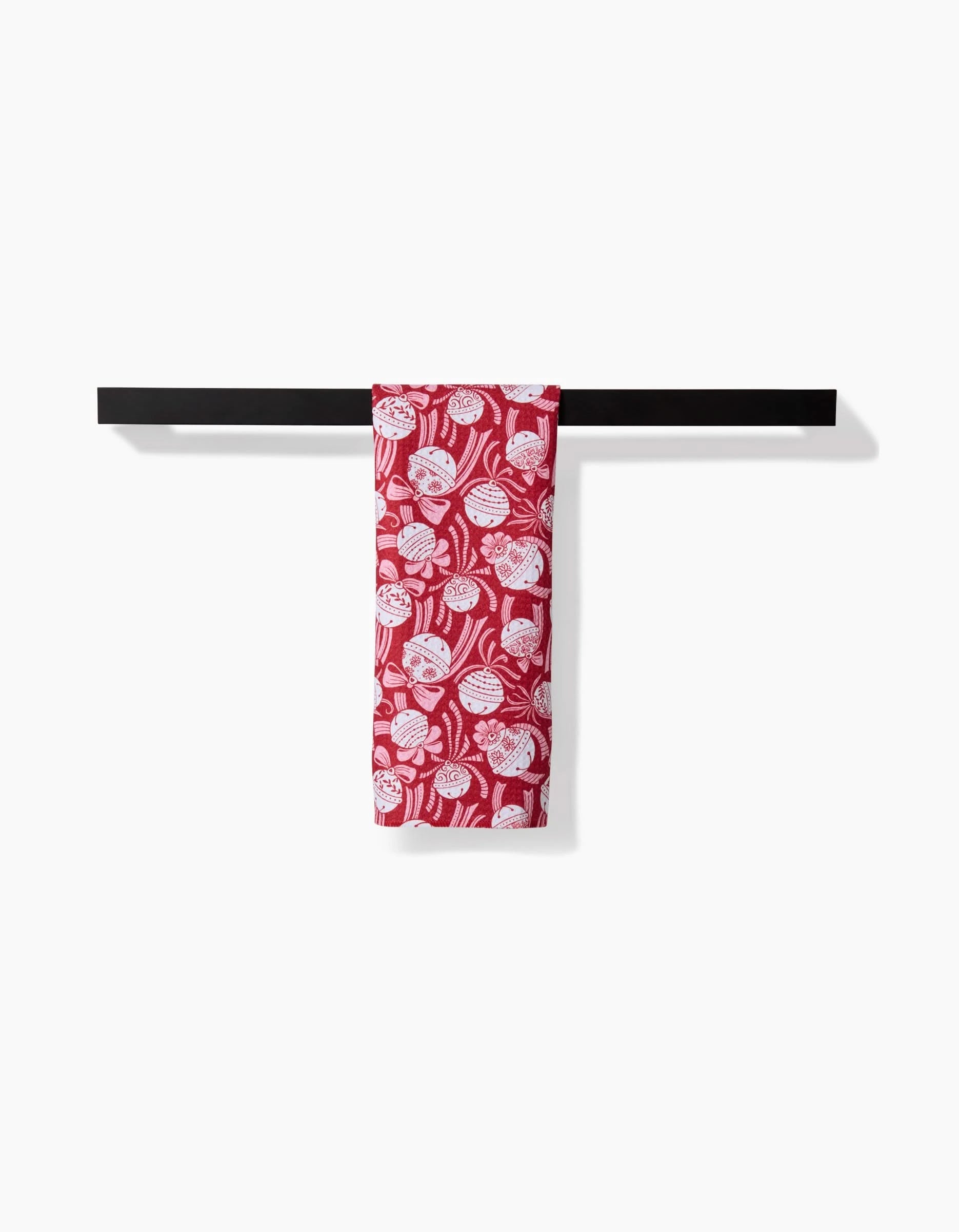 The Sarah Daugherty Holiday Bells Bows towel, ultra-absorbent and red with a white floral pattern, is neatly draped over a black towel bar against a plain white background.
