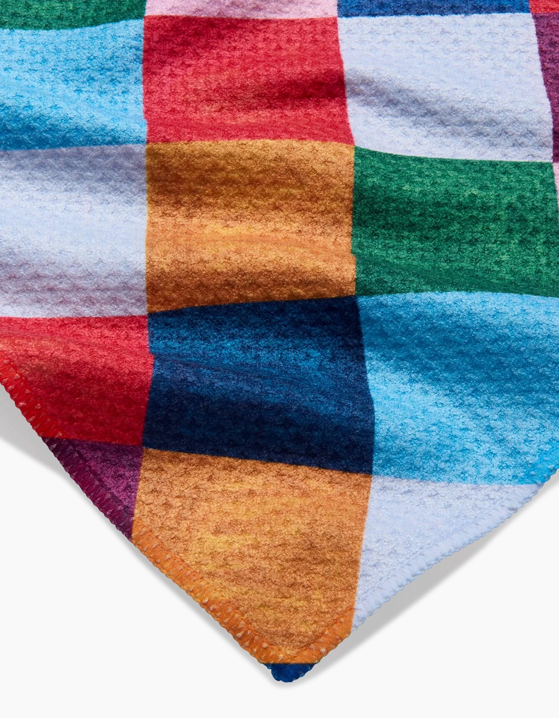 A close-up of the Holiday Harlequin recycled kitchen towel by Daria Solak, featuring textured, checkered squares in vibrant colors with an ultra-absorbent fabric and a pointed corner, set against a white background.