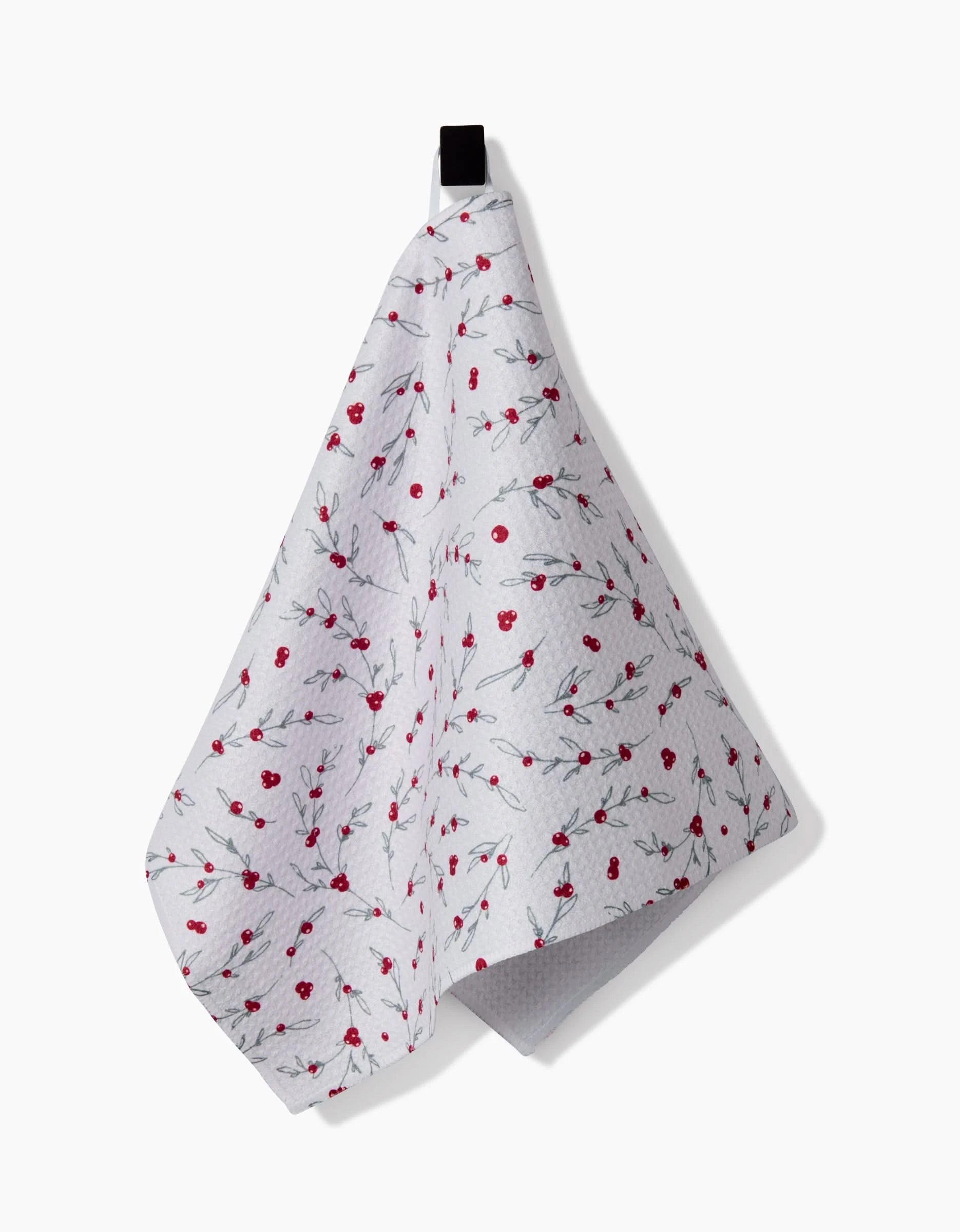 The Ashley Celena Holiday Sprigs towel, featuring ultra-absorbent white fabric with red cherry and green leaf accents, hangs from a black loop—ideal as a festive kitchen or bar towel.