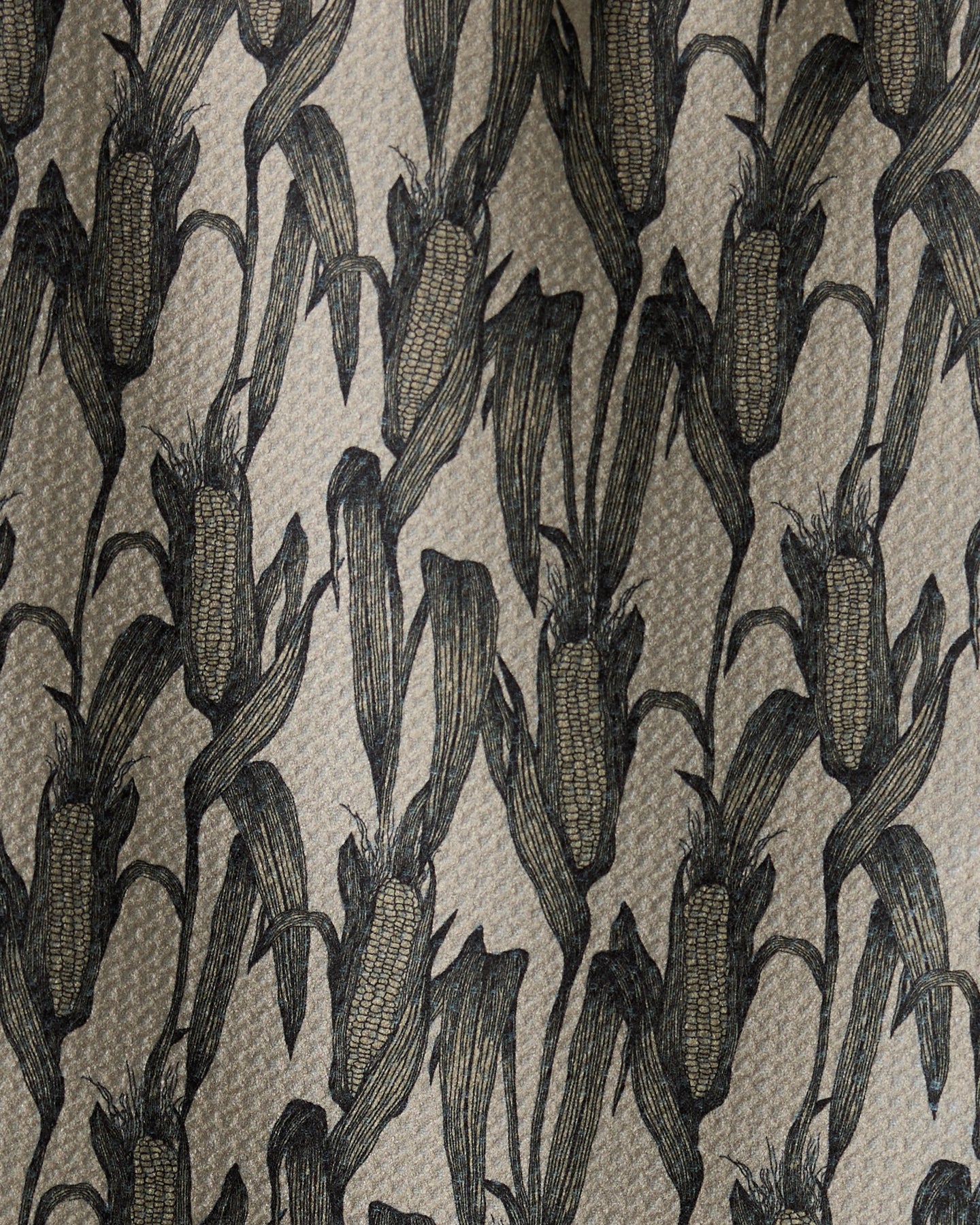 Close-up of Husk, a bar towel by Geometry, featuring a repeating pattern of black corn cobs and leaves on a beige background. The illustration-style design highlights intricate details. Made from recycled materials.