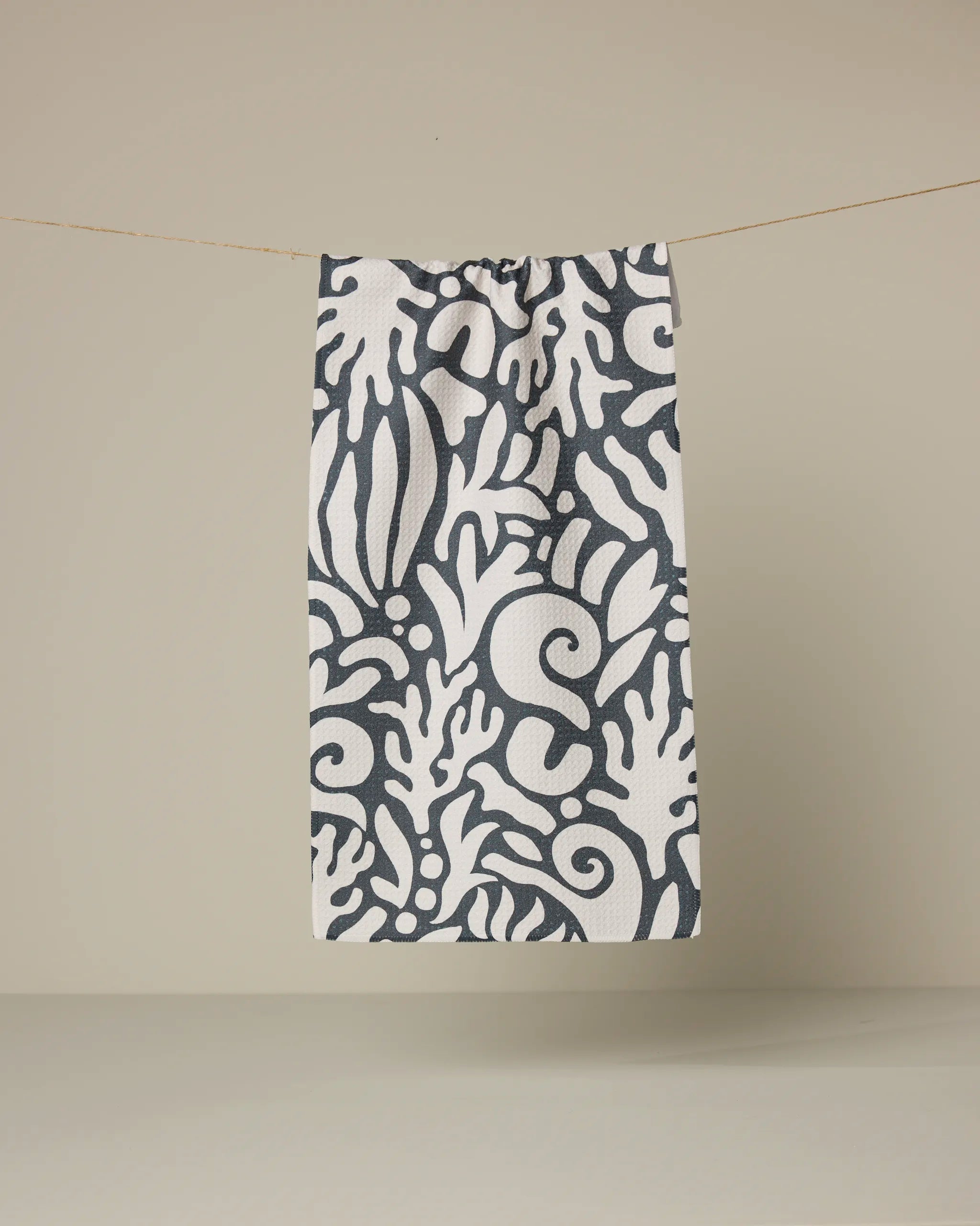 The Geometry Inkwell Reef features a rectangular white recycled fabric with a bold dark gray floral and leaf pattern, hanging vertically from a thin string against a neutral beige background.