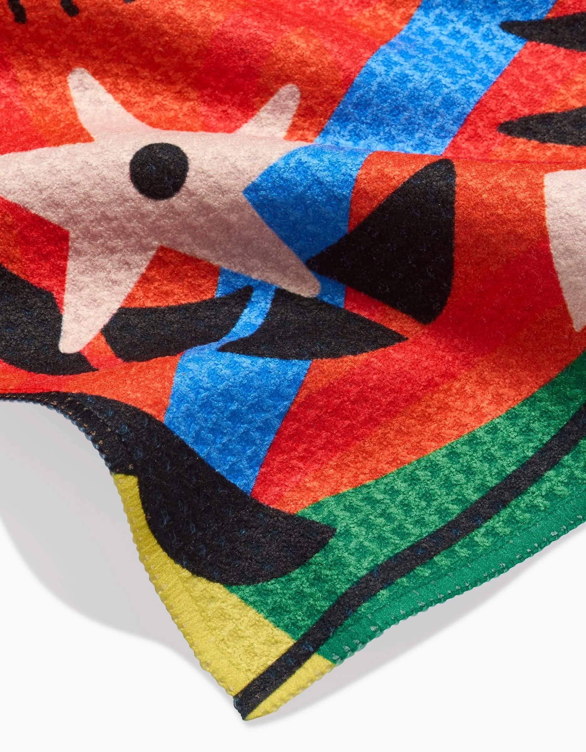 The Jacaré Bar Towel by Camila Leão features Geoweave fabric with abstract patterns: a white star with a black dot, blue diagonal stripe, black shapes, and vibrant yellow, green, red, and orange edges.