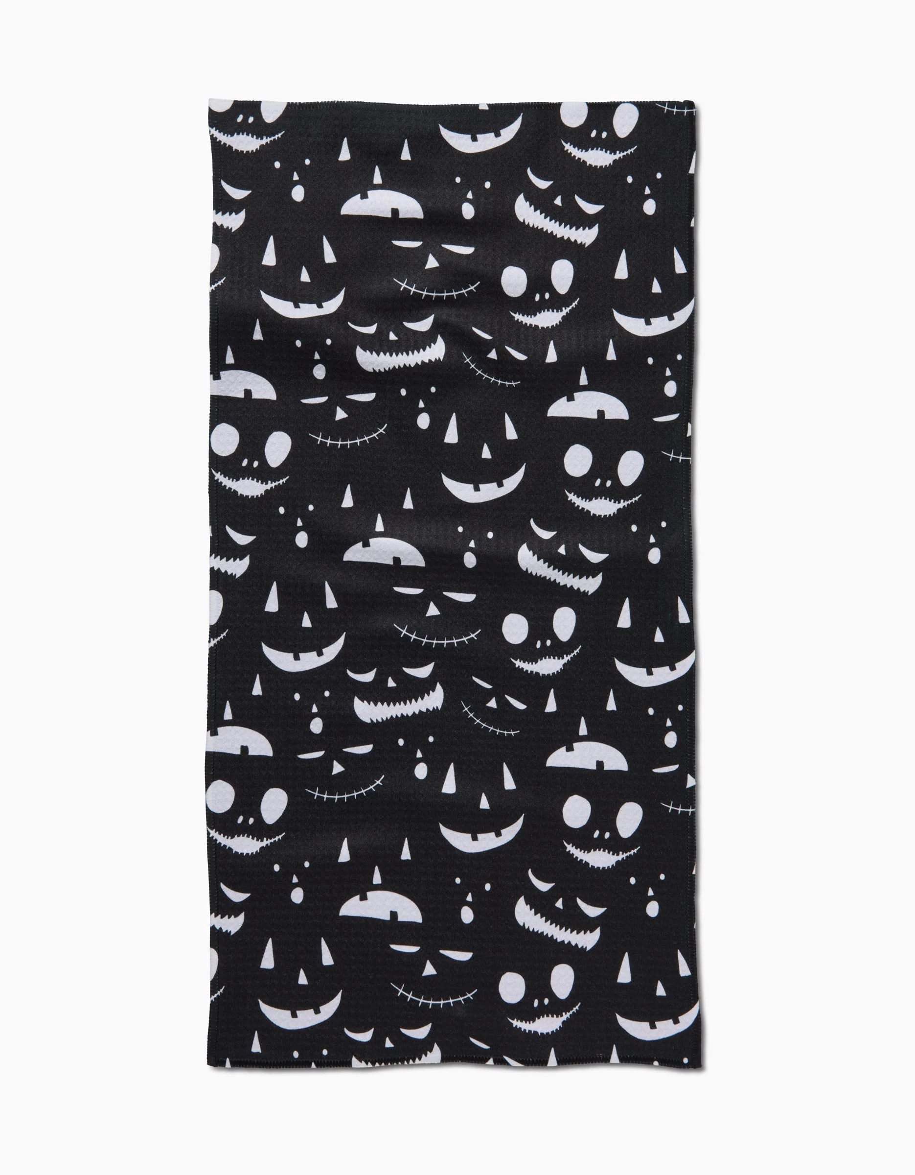 The Danelys Sidron Jack O Lantern Jamboree Black bar towel features a black fabric adorned with a pattern of various white, spooky jack-o-lantern faces with different expressions across the surface.