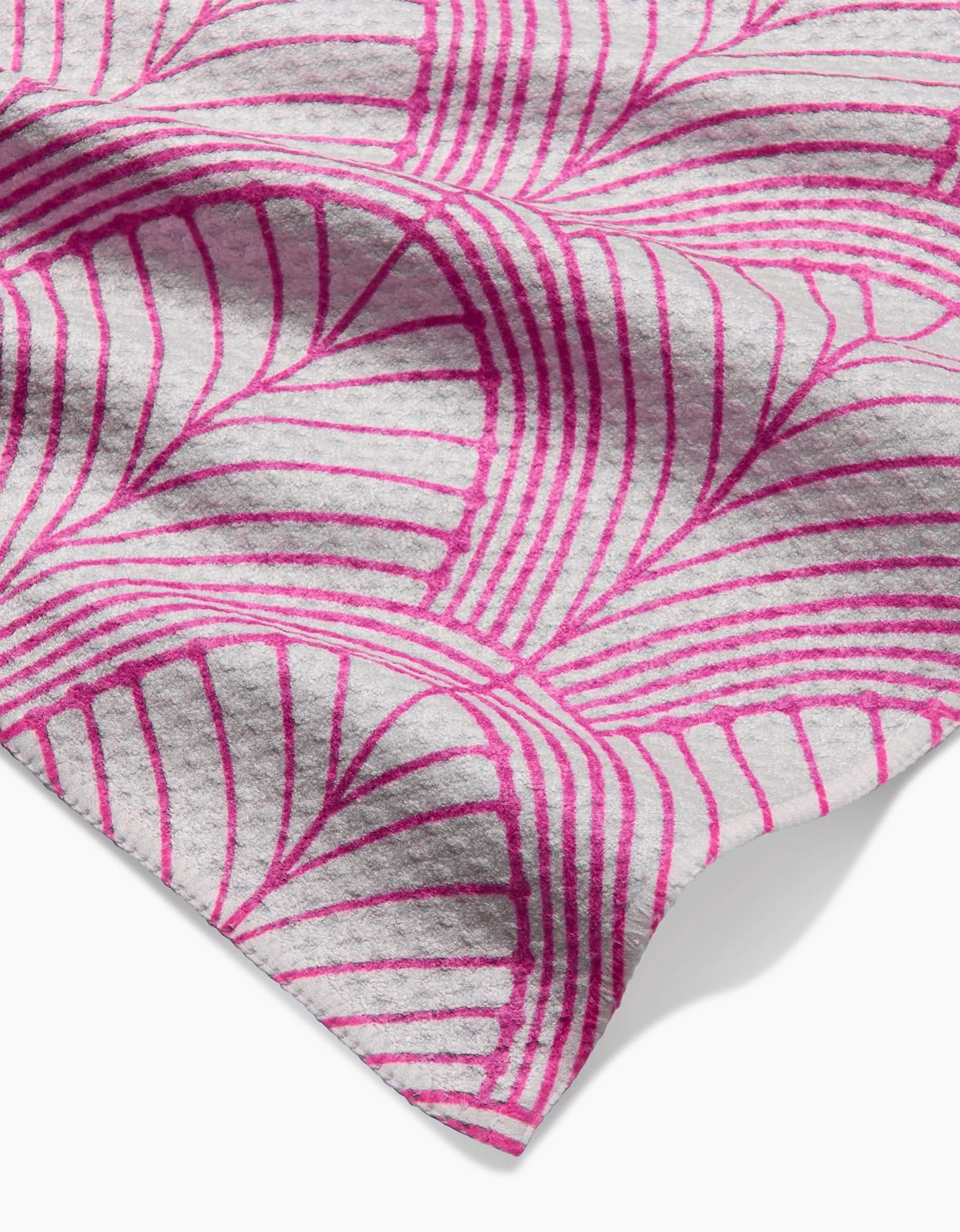 A close-up of the Jaskin bar towel by Amy MacCready, made from soft Geoweave fabric, shown on a white background with a pink and gray geometric fan or leaf pattern of curved lines and shapes. The fabric appears slightly folded.