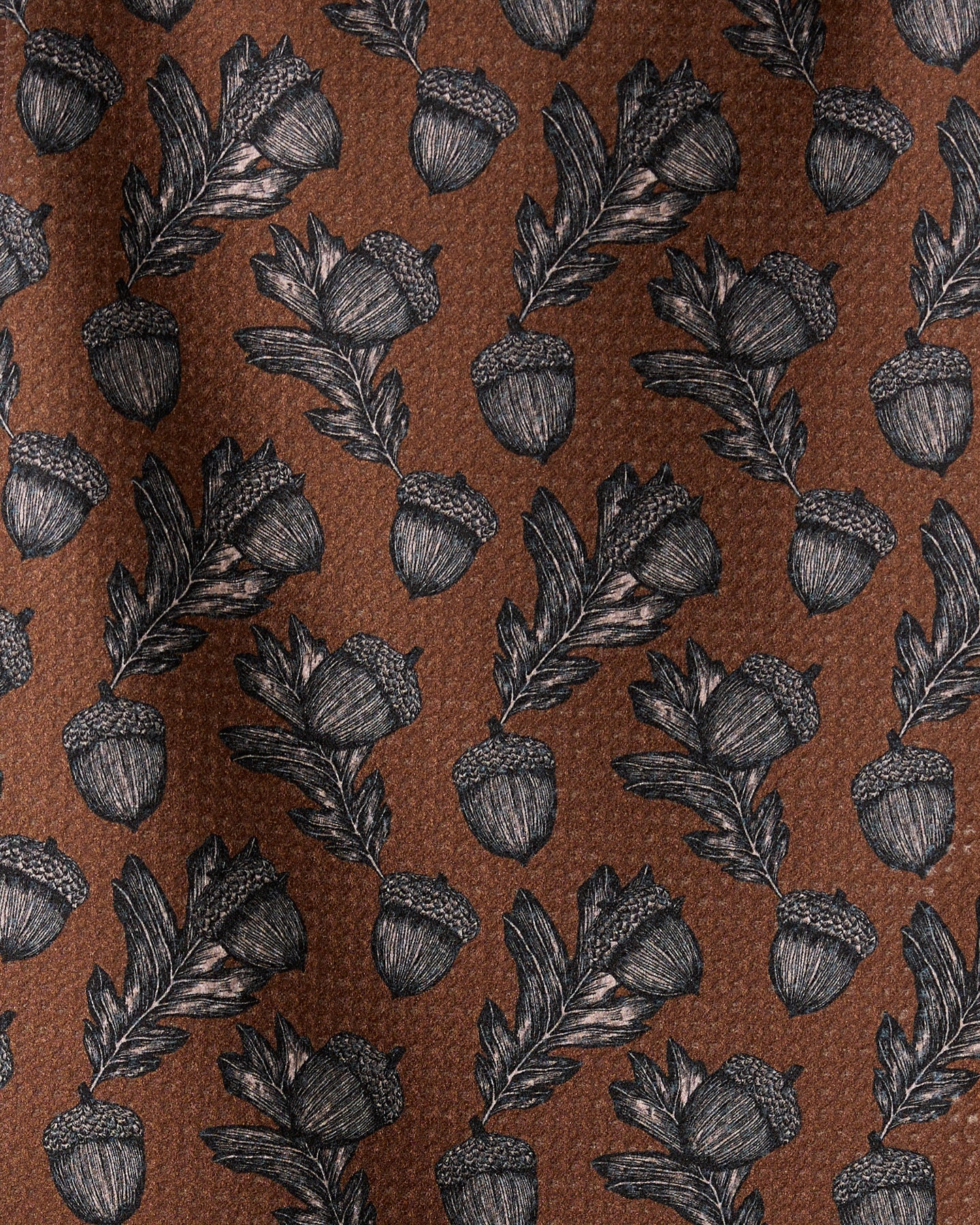 The Geometry Kindred bar towel features a brown fabric with black and white acorn and oak leaf illustrations in a repeating design, and is crafted from recycled materials.