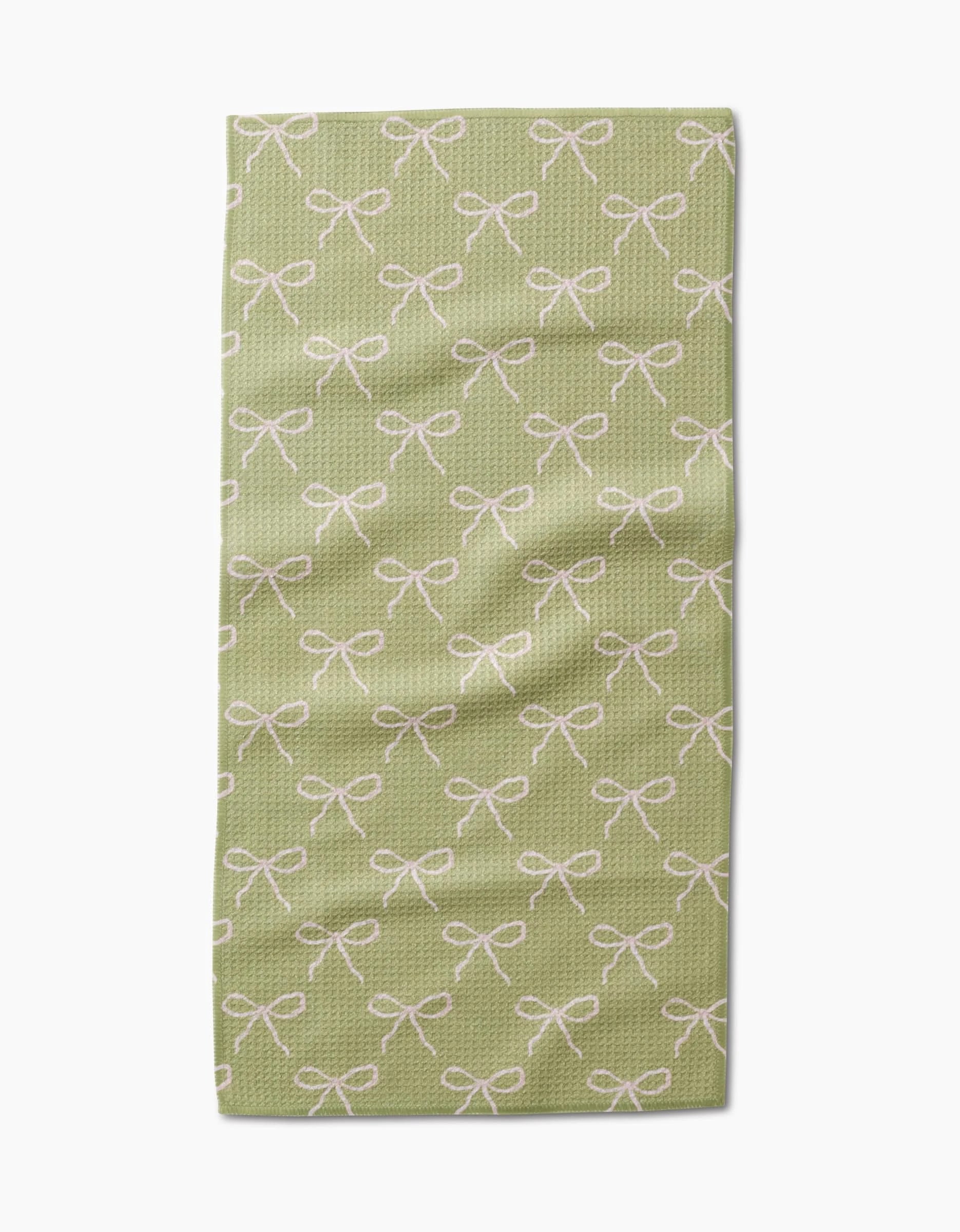 The Laura Prietto Lattice Bows bar towel is light green, made with ultra-absorbent textured Geoweave fabric, and features a repeating pattern of white bows.