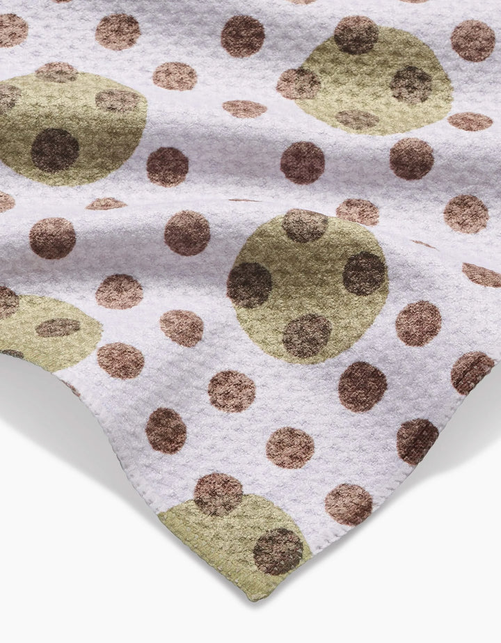 The Lotty Dotty bar towel by Studio Jeannot features a white ultra-absorbent Geoweave fabric with large olive green and small brown overlapping polka dots, elegantly draped for a stylish touch.