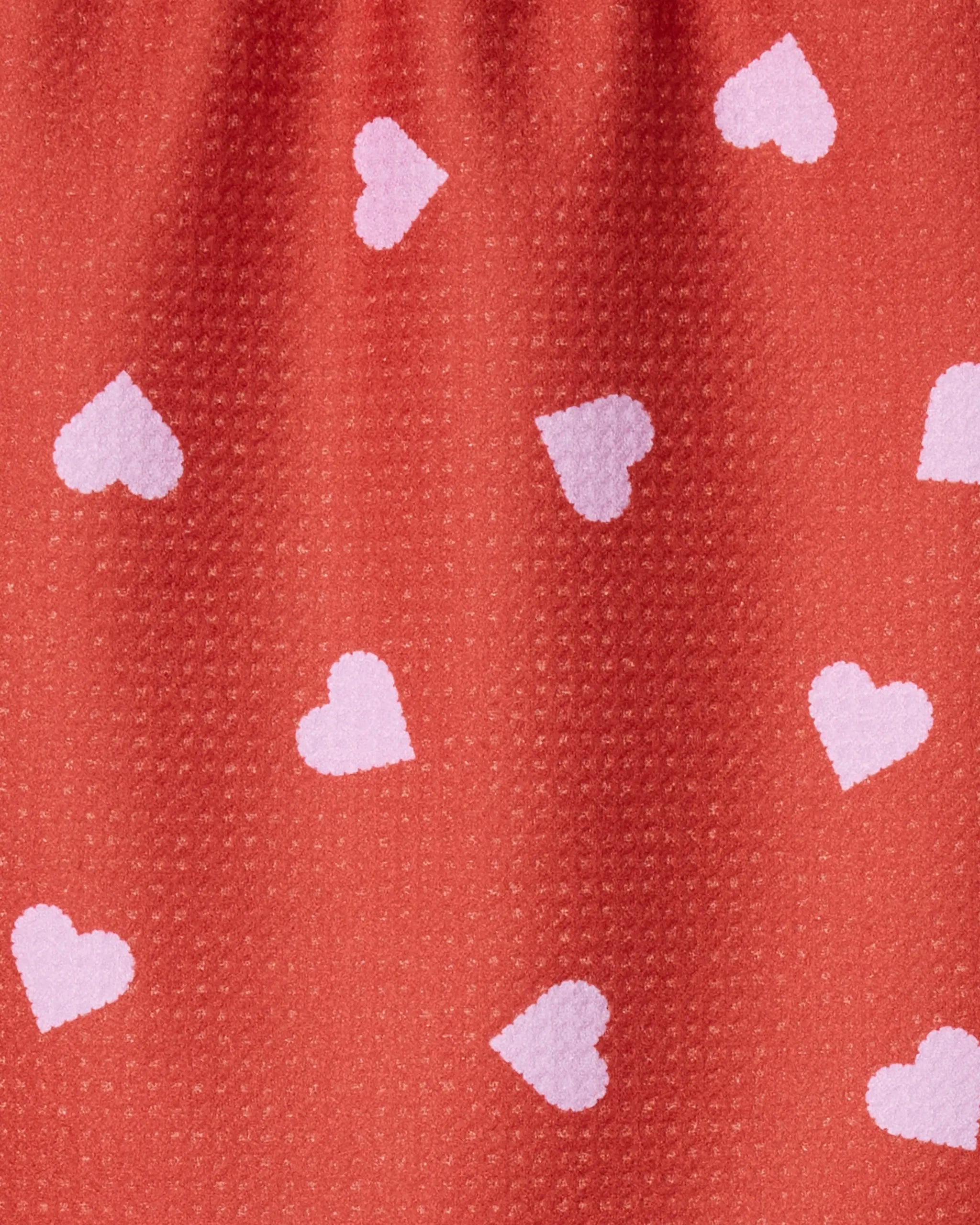 Close-up of Geometry's Love Toss towel, a red ultra-absorbent piece made from recycled materials with light pink heart shapes scattered across its textured surface.