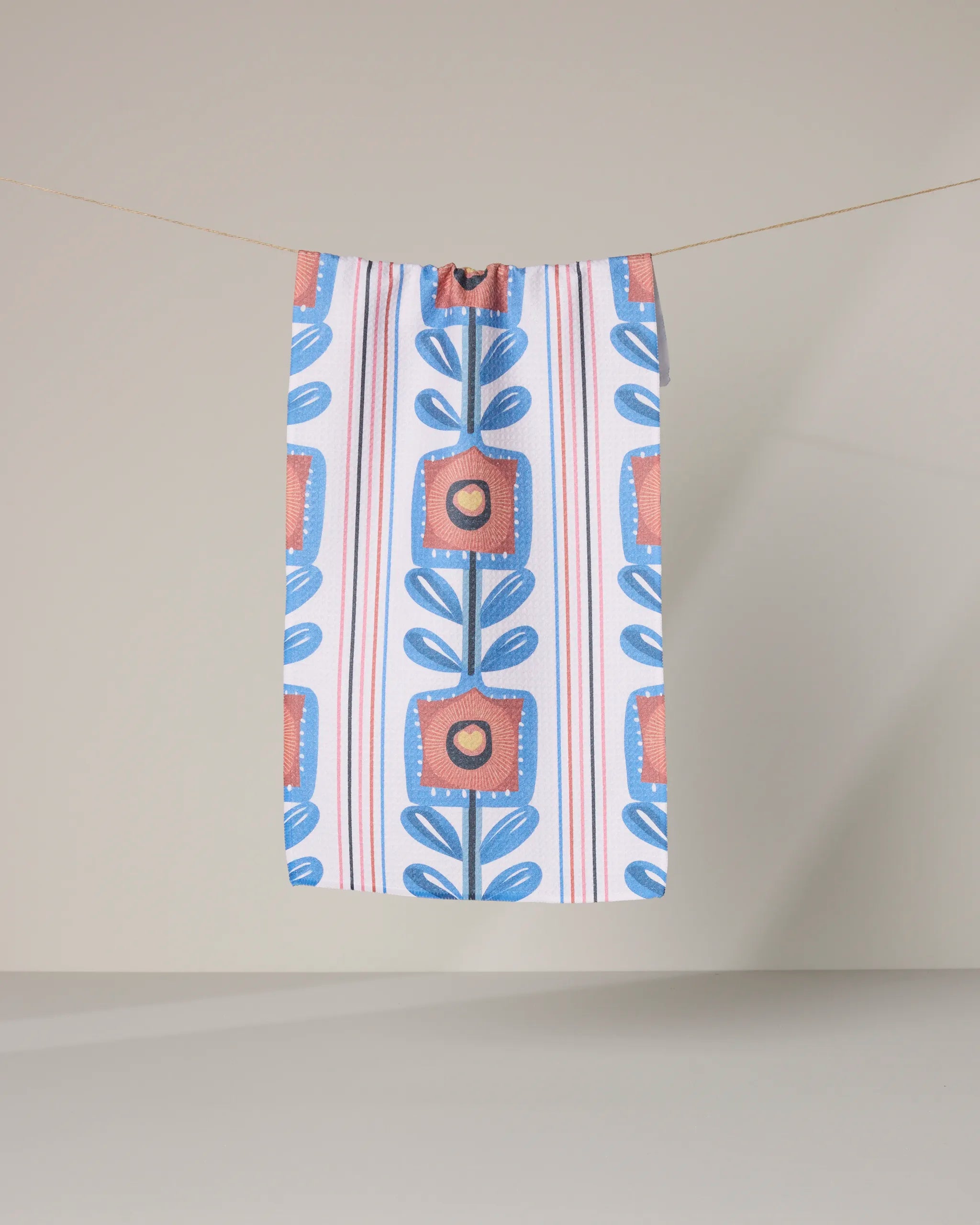 The Geometry Lovestack rectangular bar towel, featuring a bold blue, orange, and red geometric floral design, hangs on a string against a neutral background.