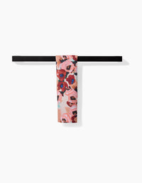 The Lucia towel by Ania Zwara Art, featuring a floral pattern in pink, red, and blue tones, hangs neatly on a simple black horizontal rack against a plain white background.