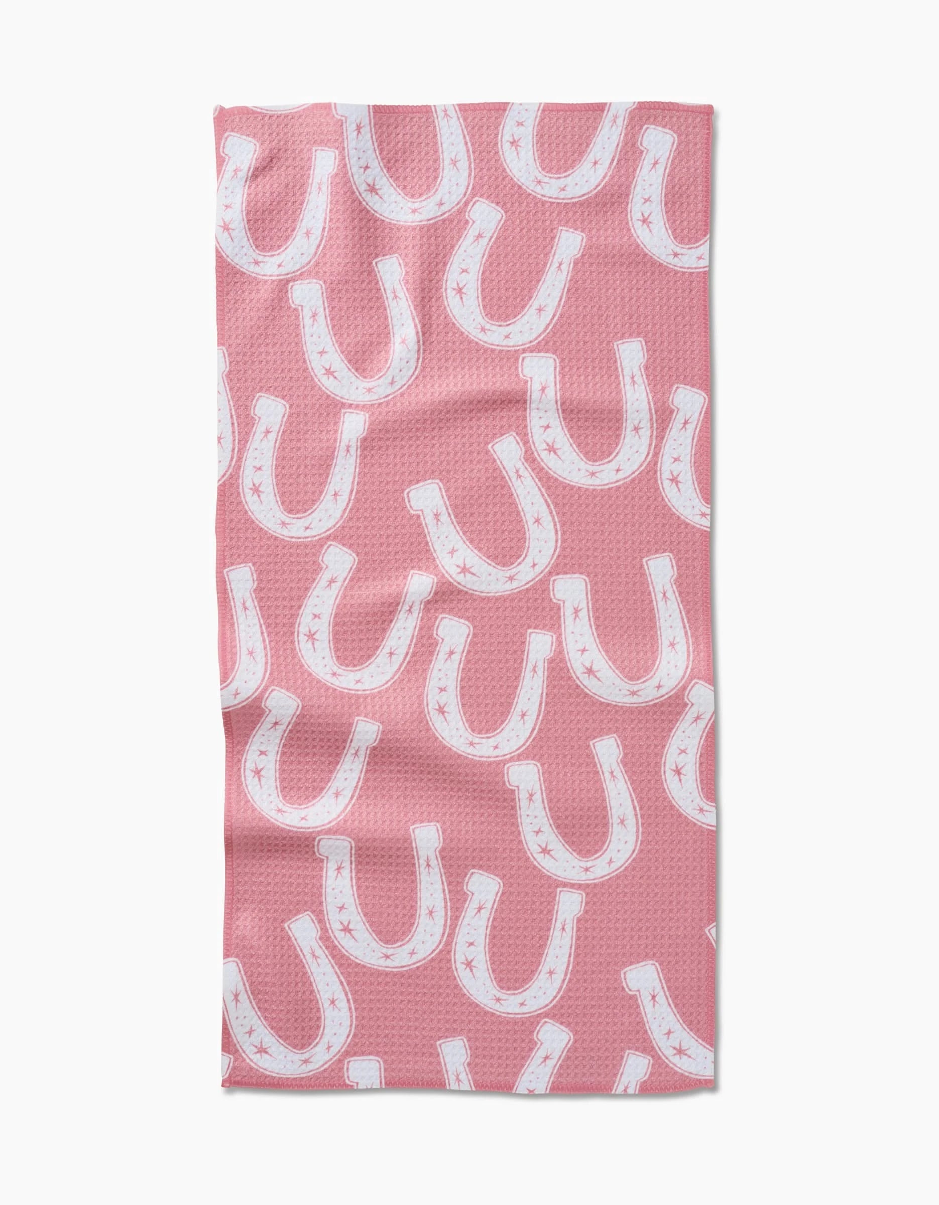 The Aubrey Fairchild “Lucky Horseshoe” bar towel features a pink Geoweave fabric with a repeating white horseshoe and subtle star pattern in various orientations.