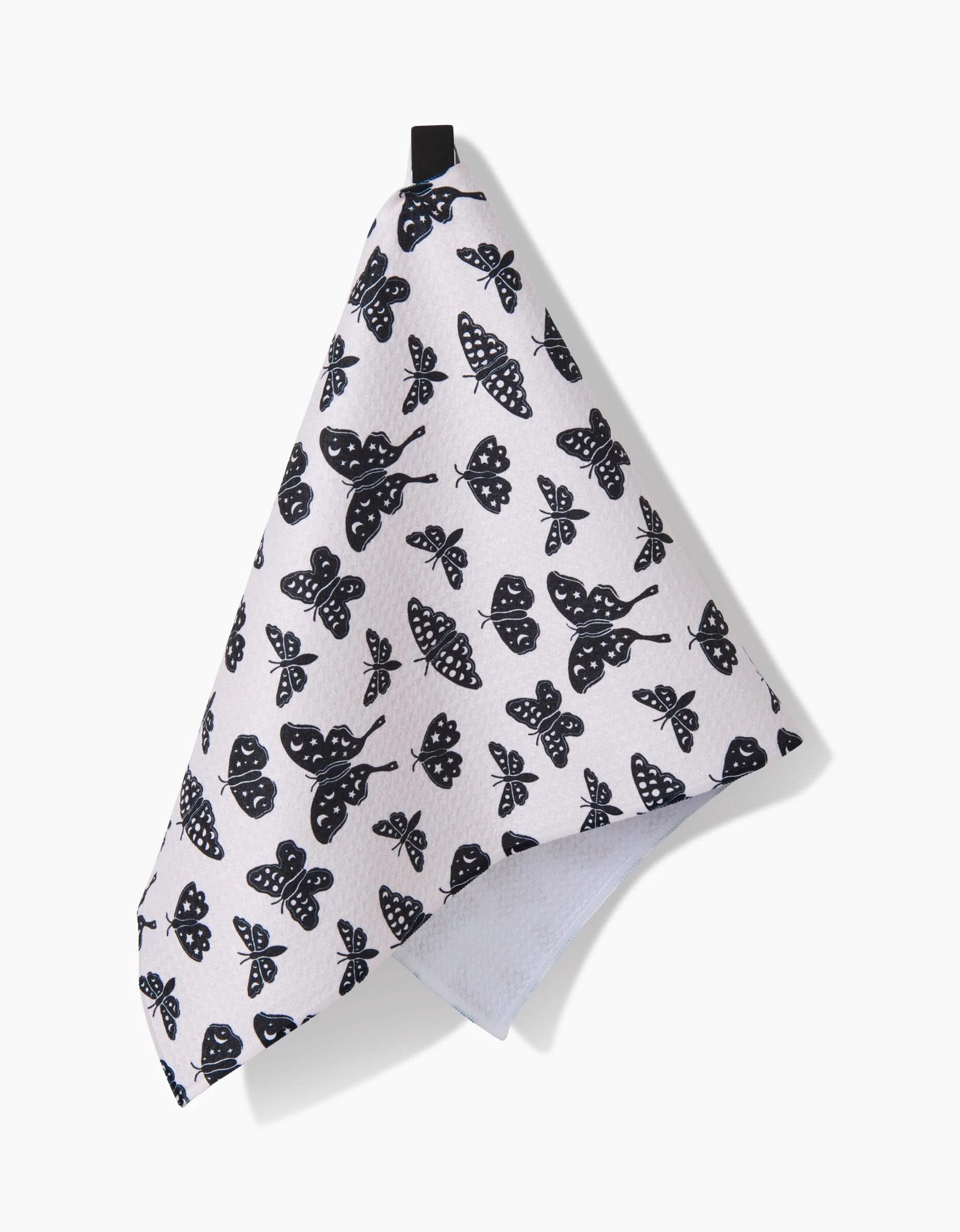 The Kayla Ann Lunar Moths White ultra-absorbent towel, featuring a black moth pattern, hangs from a black loop against a plain white background.