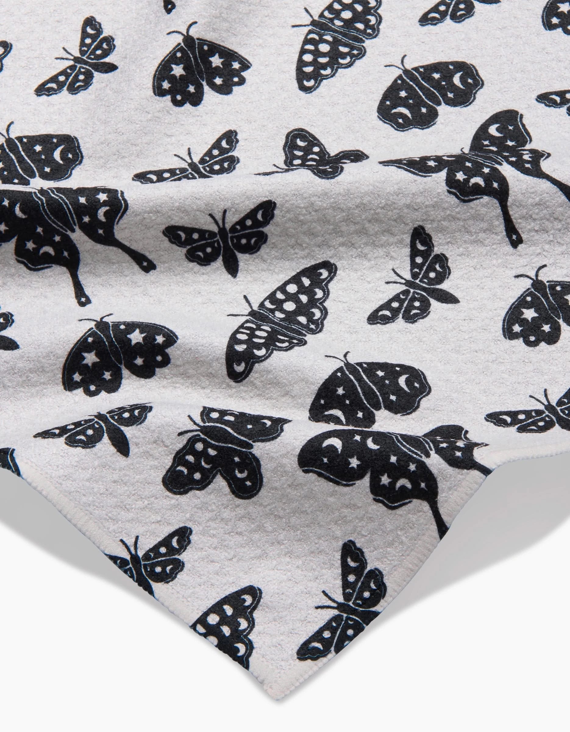 A close-up of Kayla Ann’s Lunar Moths White bar towel, made from recycled light gray fabric, features black moths with varied wing designs—spots, stripes, and solids—for ultra-absorbent style.