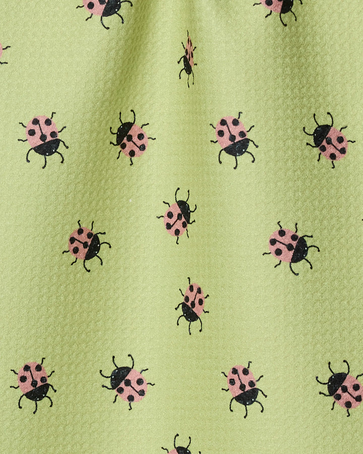 The Mariquita bar towel by Geometry features light green Geoweave fabric patterned with small pink and black ladybugs, all made from recycled materials for a playful touch.