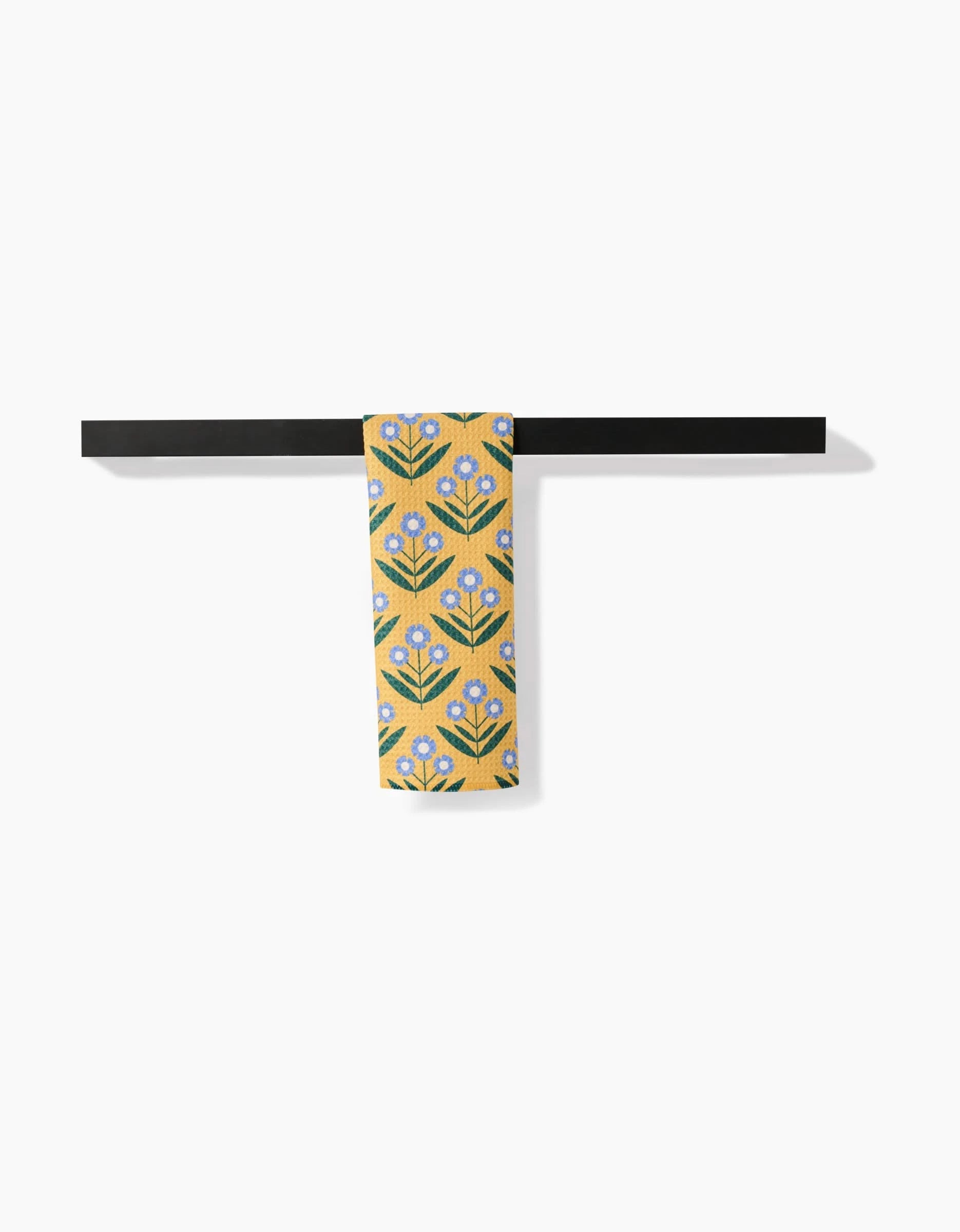 The Mayday necktie by Megan Kampa, crafted from recycled materials, features blue and white flowers with green leaves on yellow fabric. It is draped over a black bar set against a white background.
