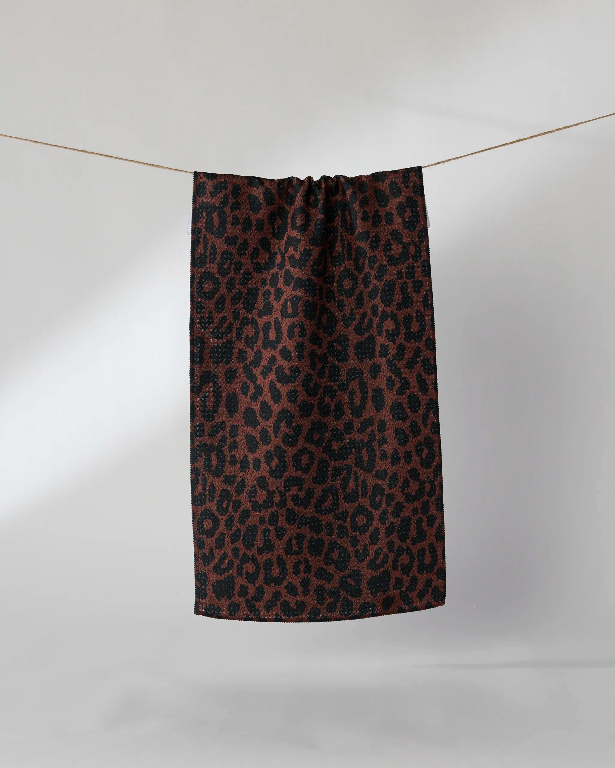 The Geometry Midnight Safari bar towel, featuring a brown and black leopard print on Geoweave fabric, hangs from a thin string against a plain light background.